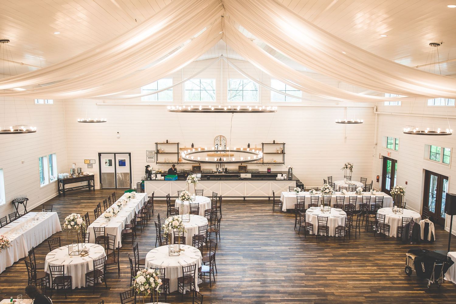 An elegant white reception hall with draped ceiling, round tables, and natural lighting.