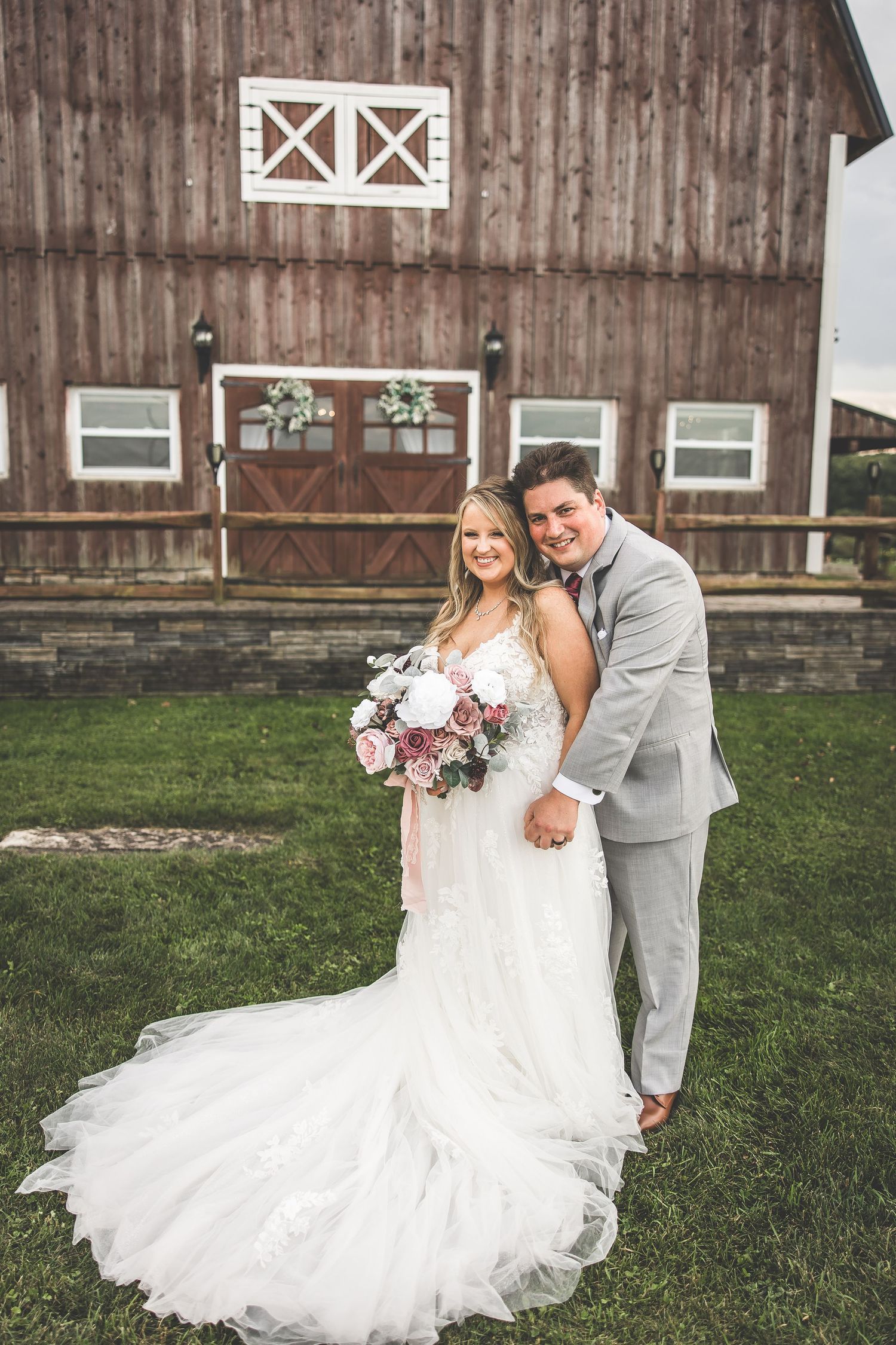 Romantic wedding portraits against rustic barn backdrop with flowing white dress.