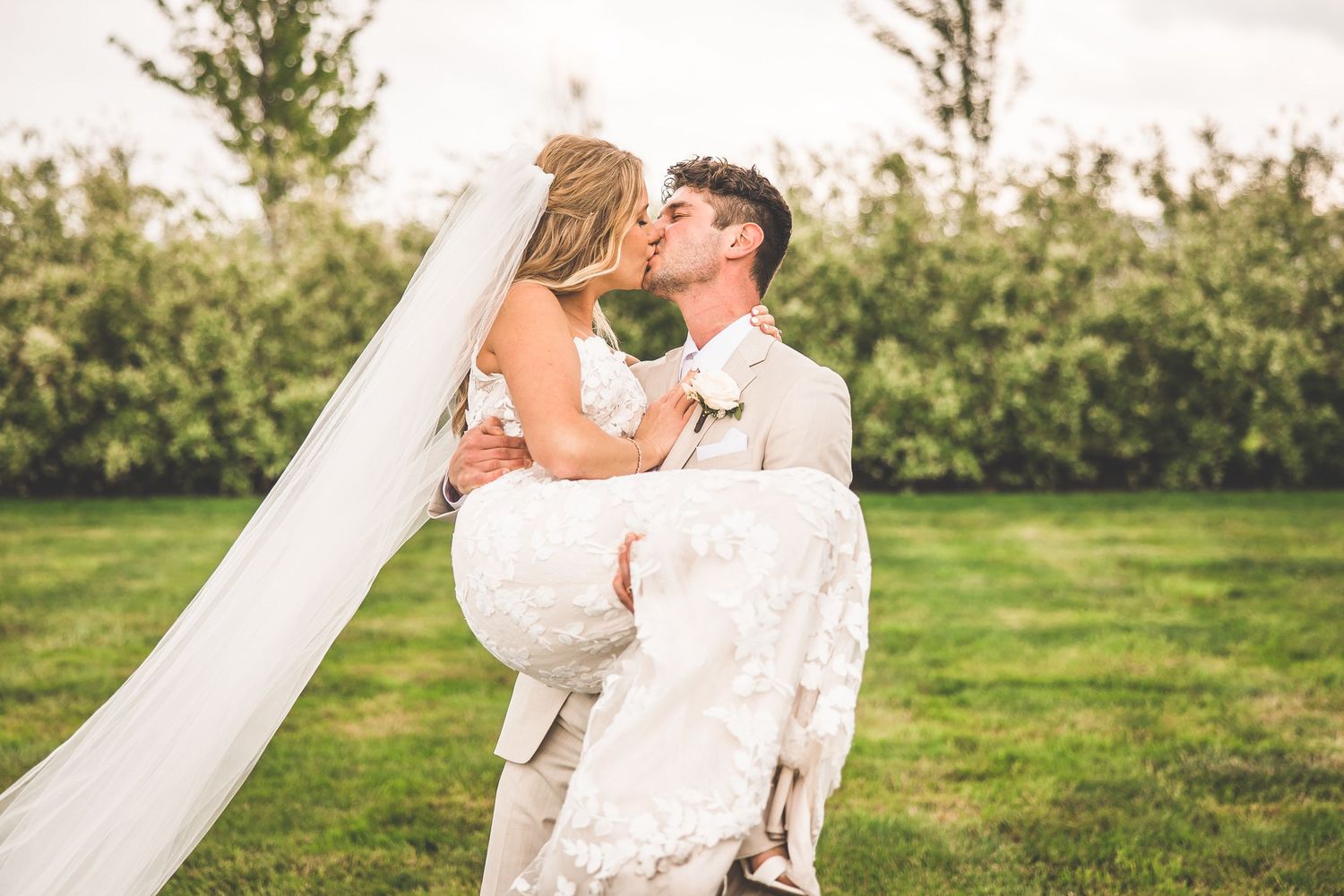 Romantic wedding portraits in a lush green field with flowing veil and natural lighting.