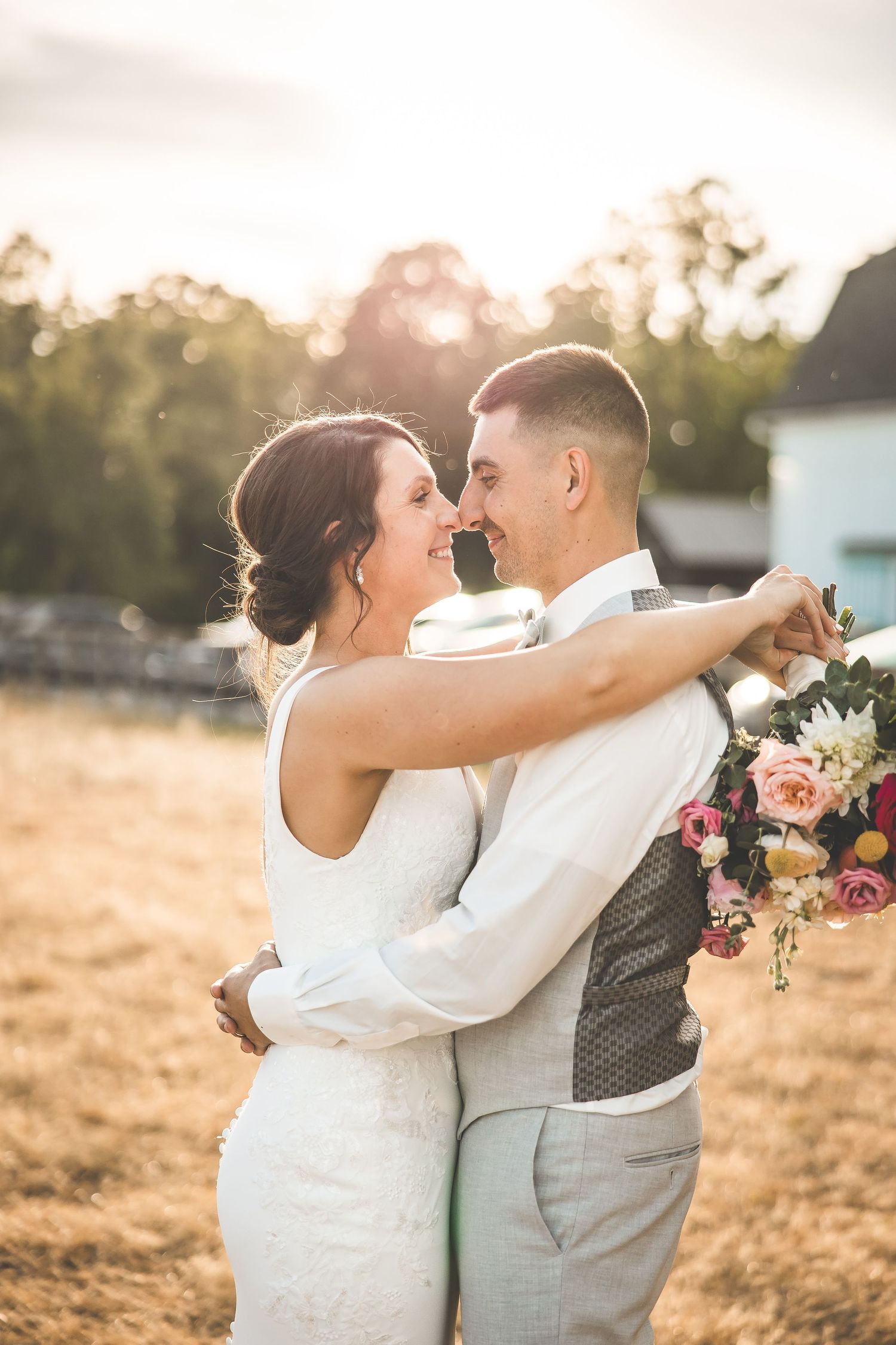 Newlyweds embrace in golden sunset light in an outdoor field setting.