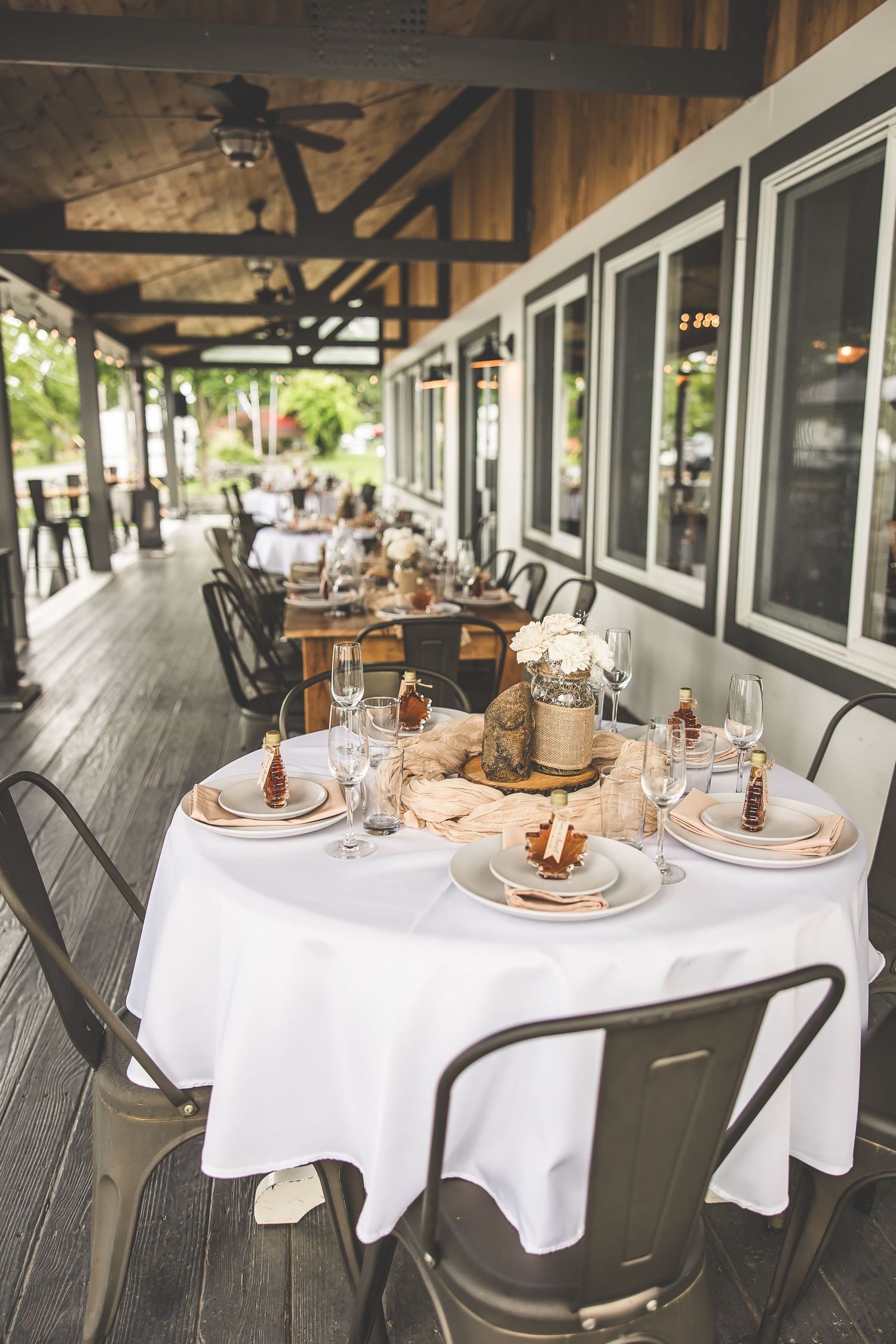 Outdoor dining area with white tablecloths and place settings on covered patio.