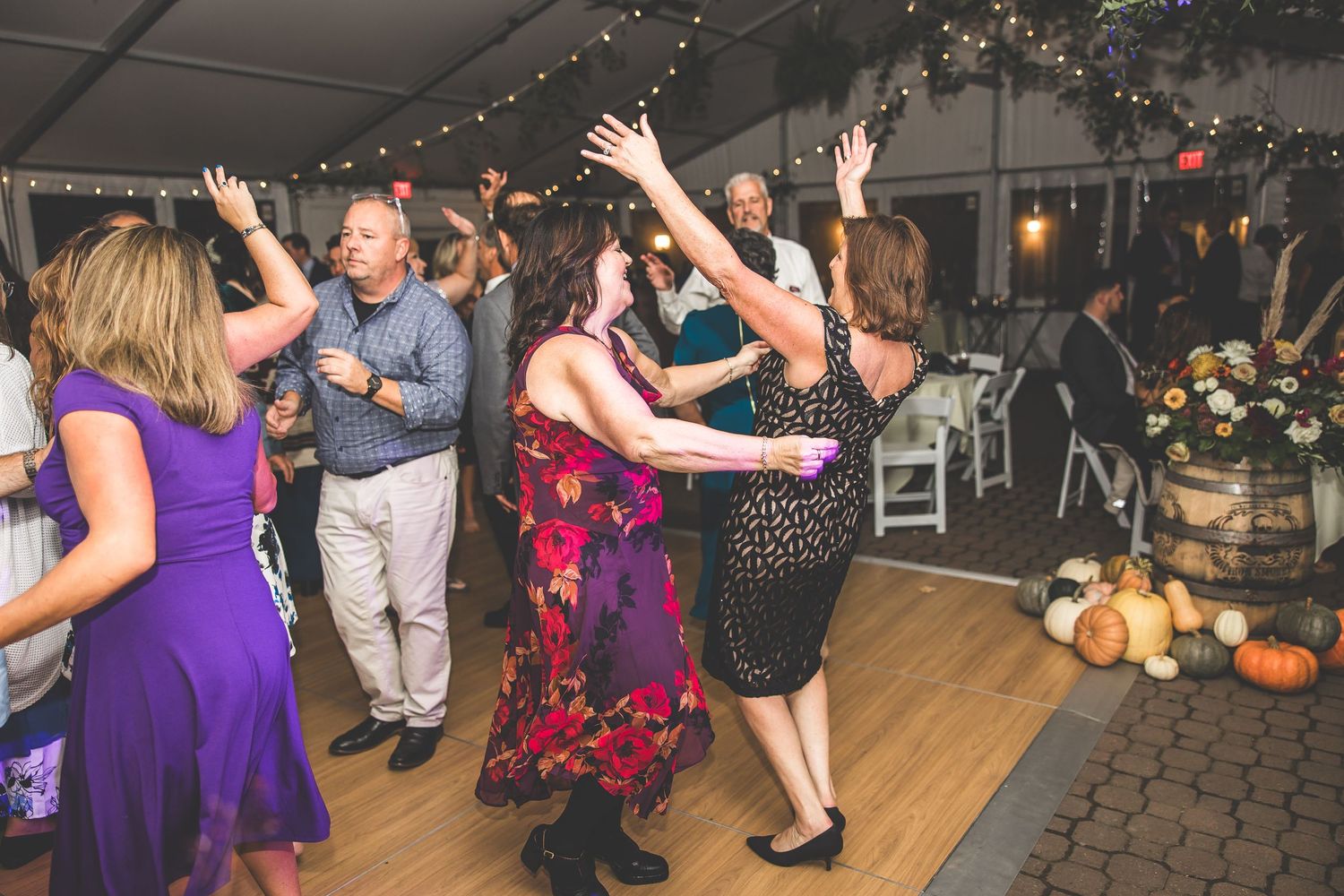Wedding guests dancing and celebrating in a decorated tent venue with string lights and fall decorations.