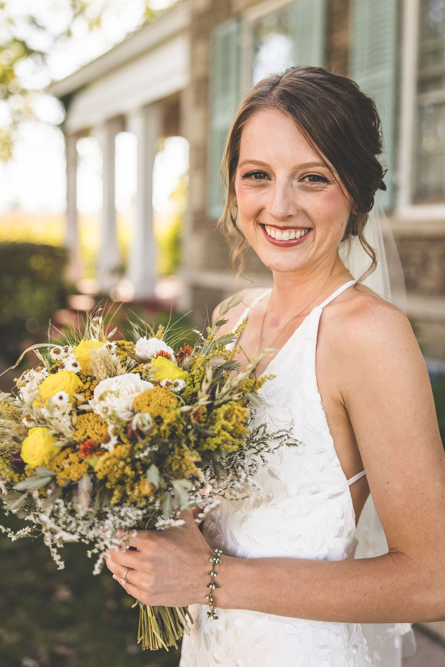 A bride holds a vibrant yellow and white wildflower bouquet while posing outdoors.