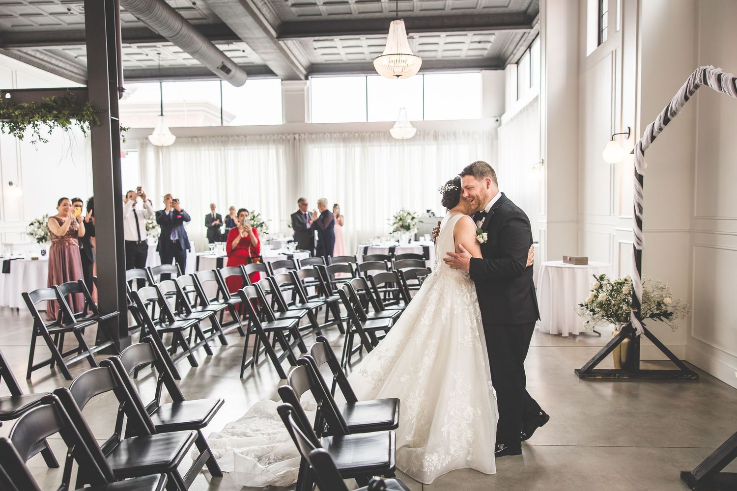 Wedding ceremony setup in bright indoor venue with rows of black chairs and natural lighting.