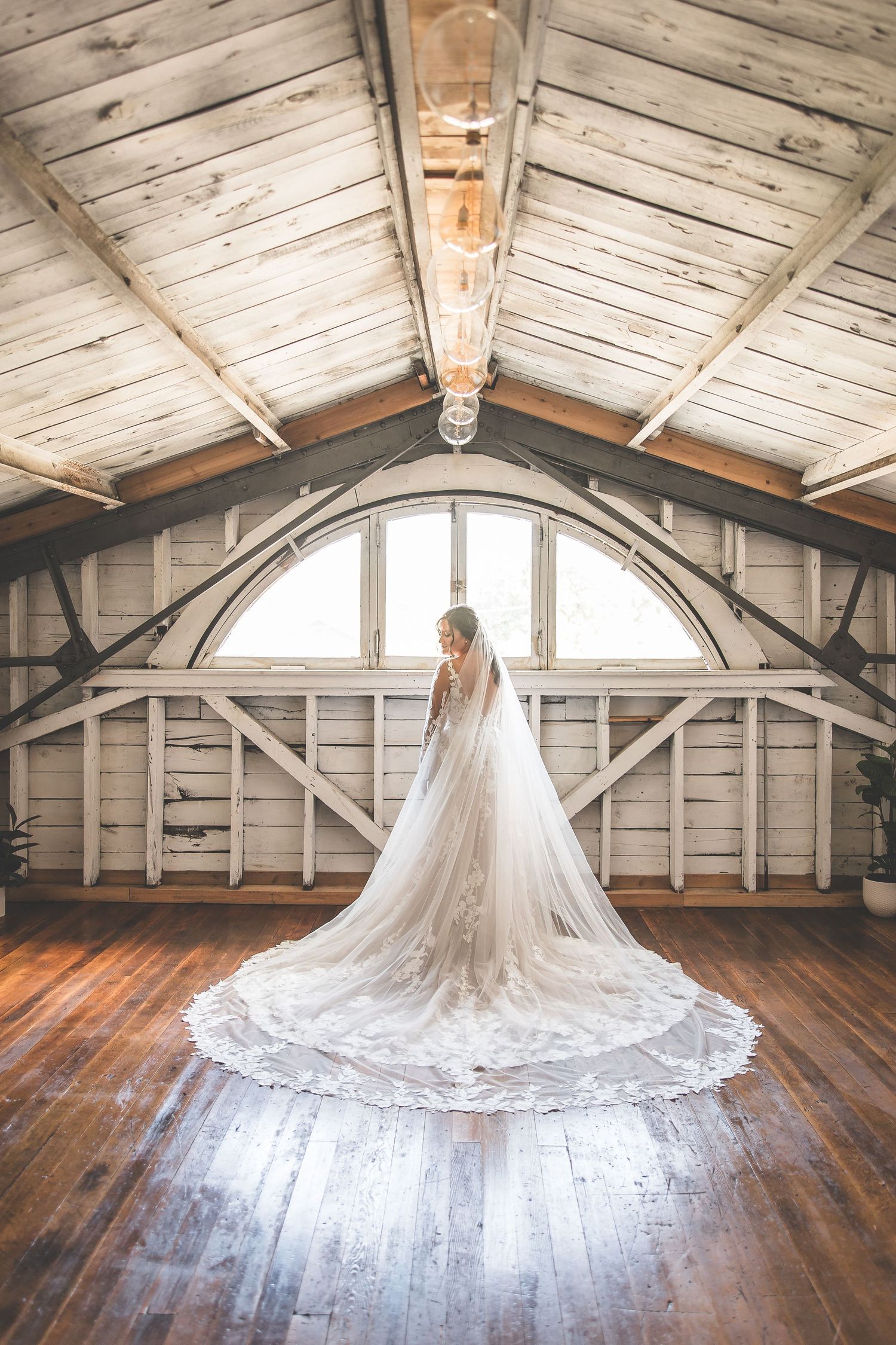 Wedding dress displayed in rustic barn venue with dramatic arched windows and wooden beams.