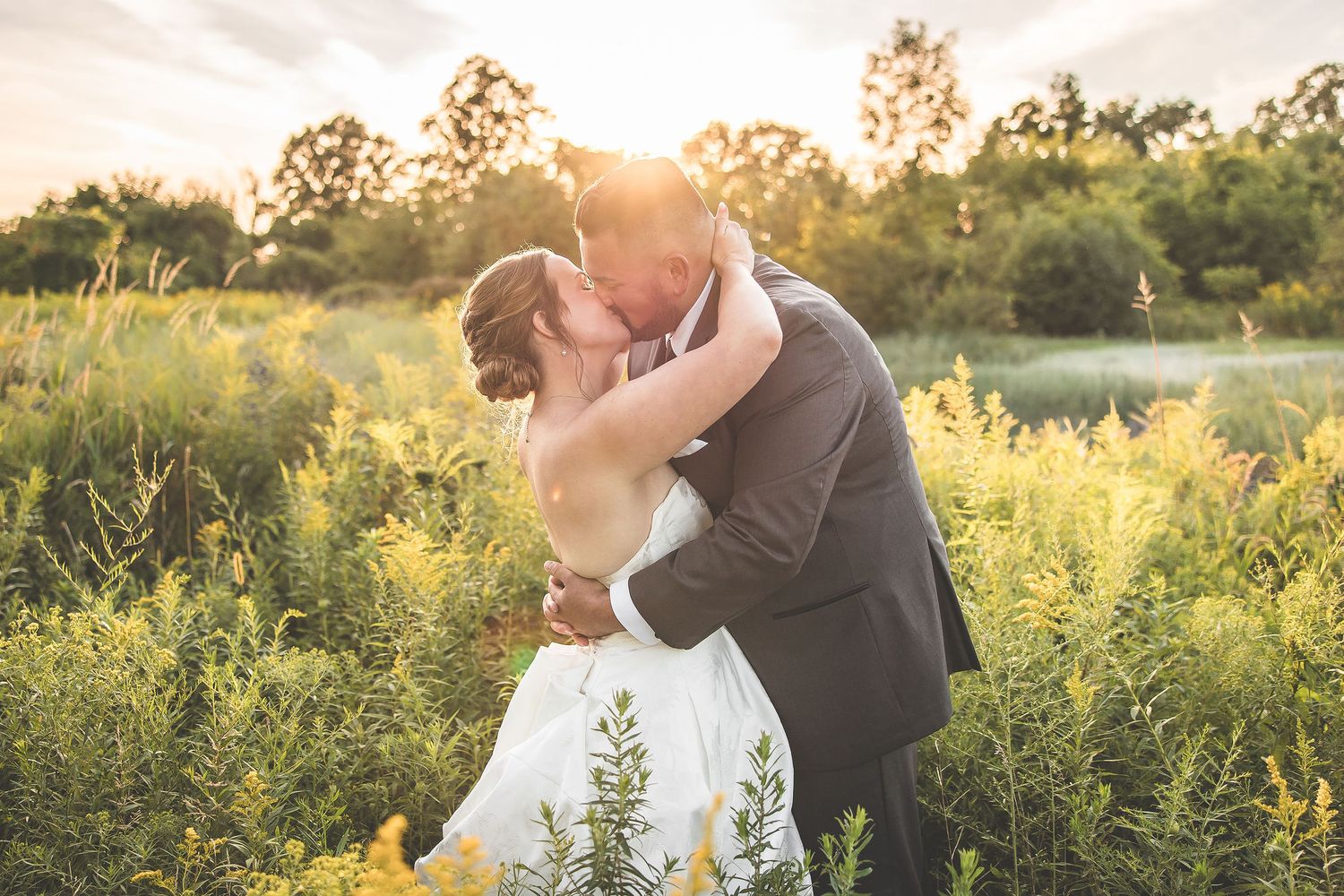 Romantic sunset wedding portraits in a field of wildflowers with golden light filtering through trees.