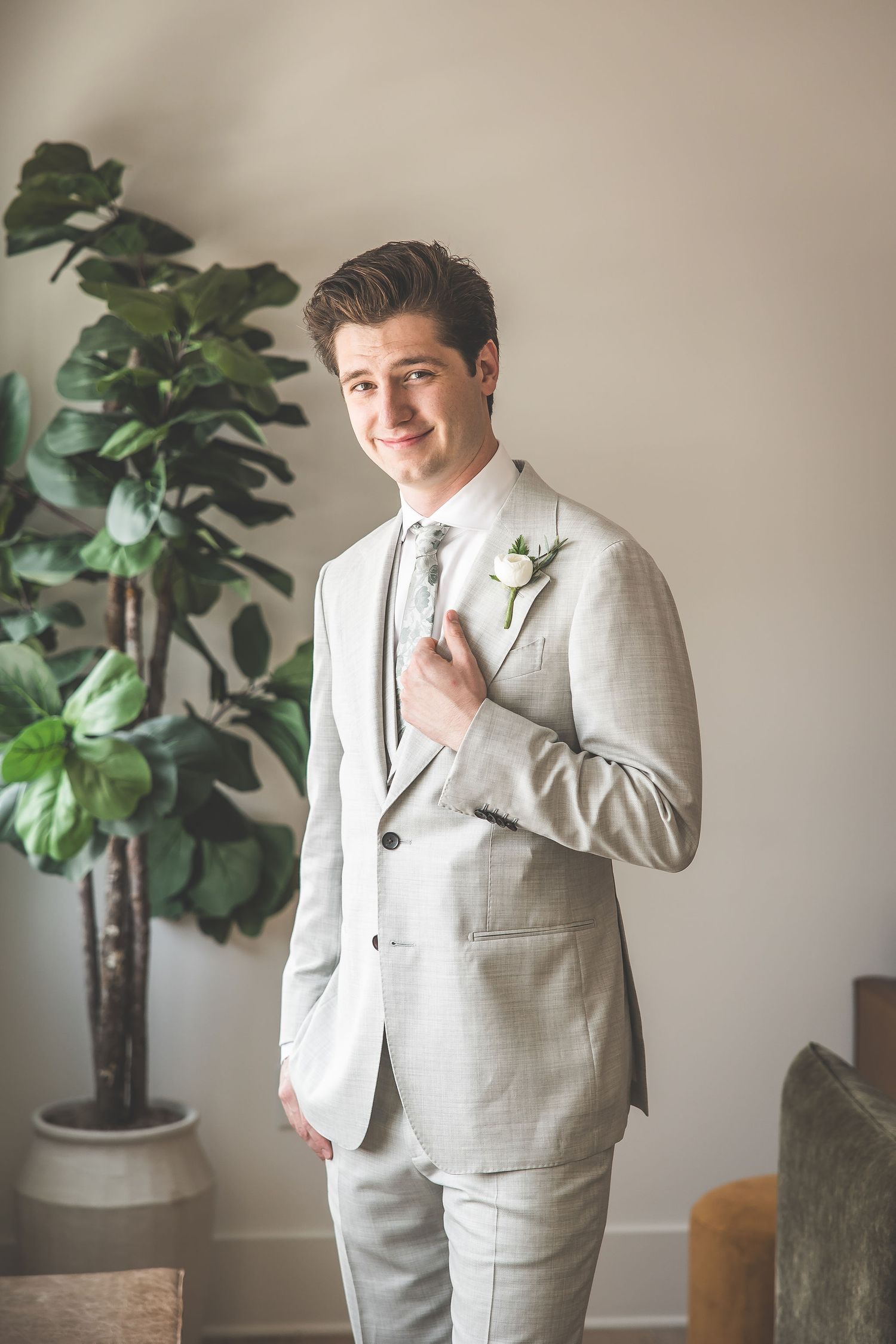 Formal portraits showing someone in a light gray suit posing next to indoor plants.