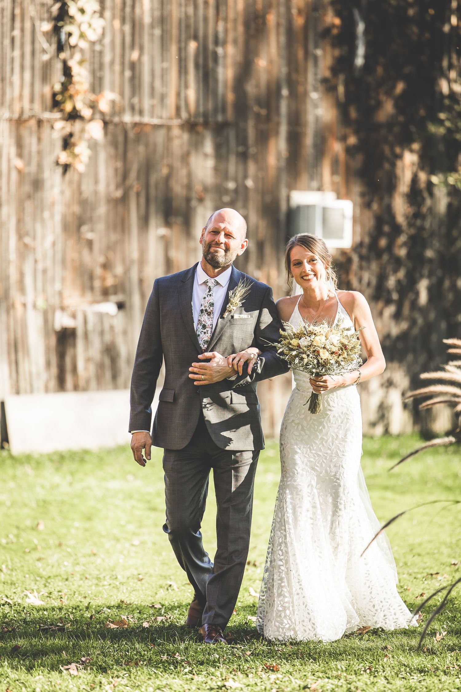 A couple walks together on their wedding day in front of a rustic barn backdrop.