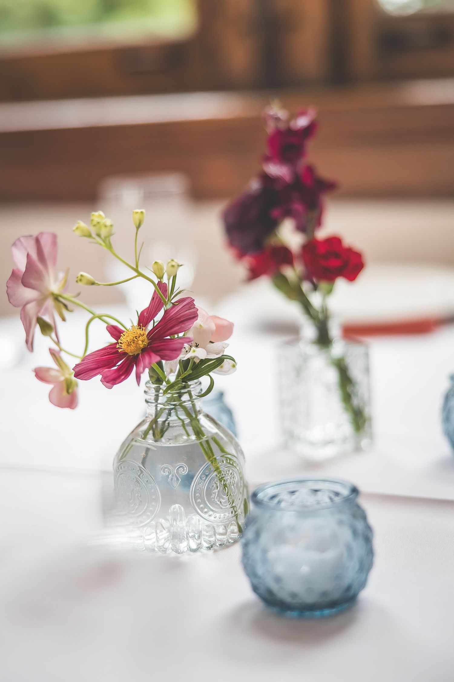 Colorful cosmos flowers arranged in blue hobnail glass vases on white tablecloths.