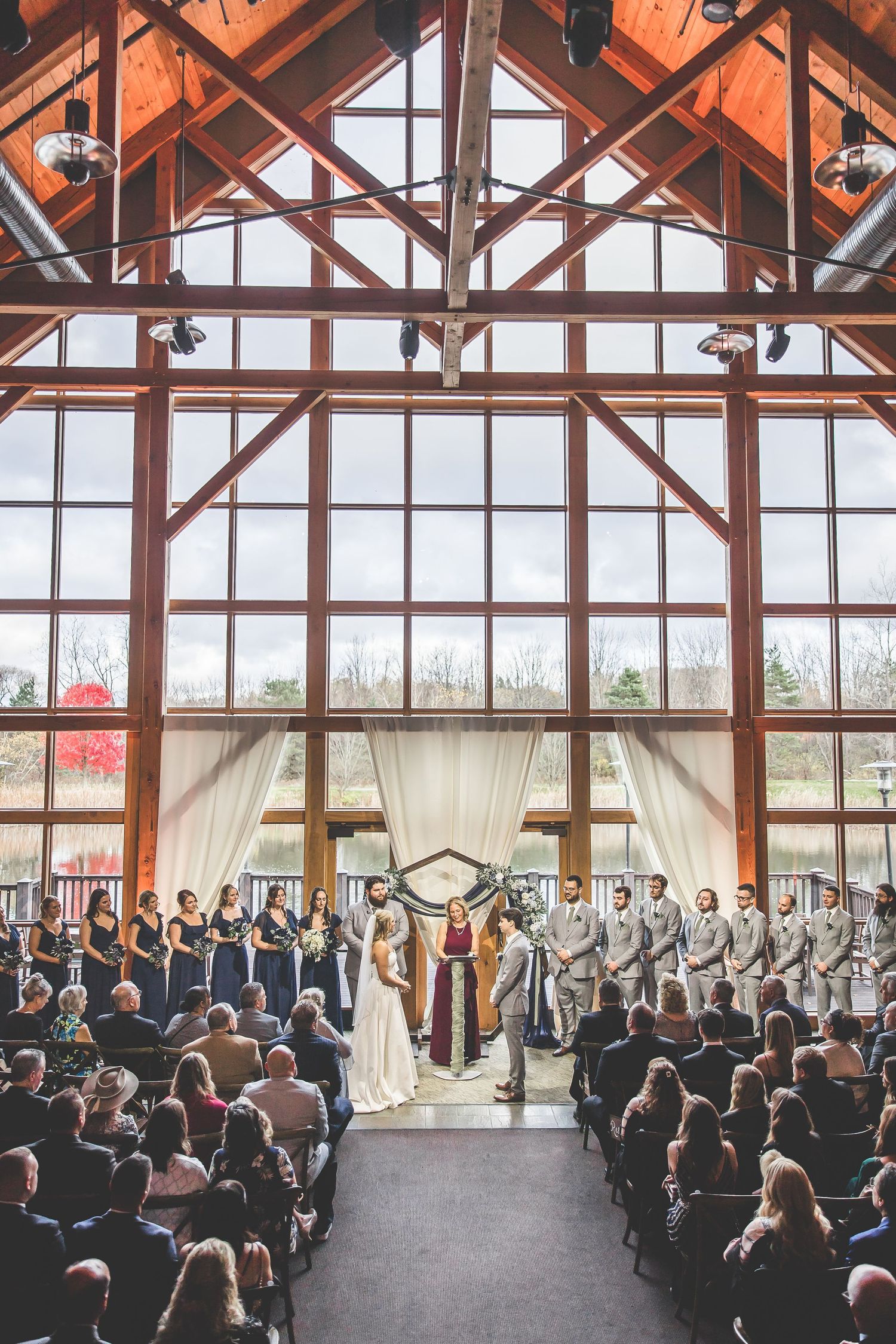Panoramic view of wedding ceremony with guests seated in rows beneath exposed wooden beams.
