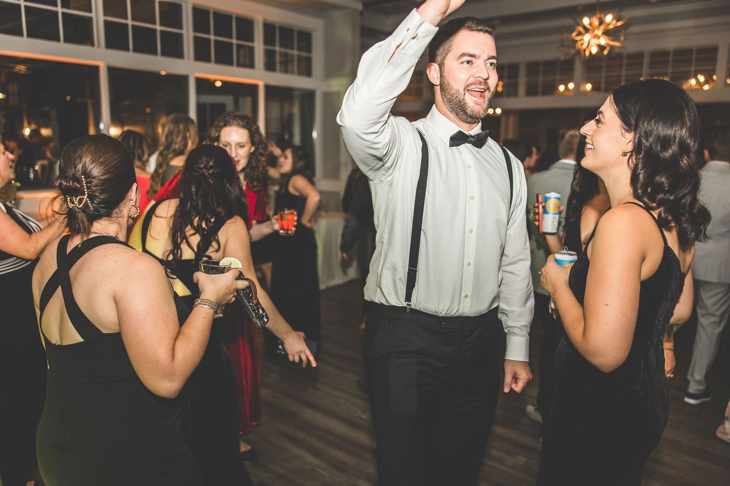 Guests dancing and having fun at a dimly lit wedding reception with decorative lighting.