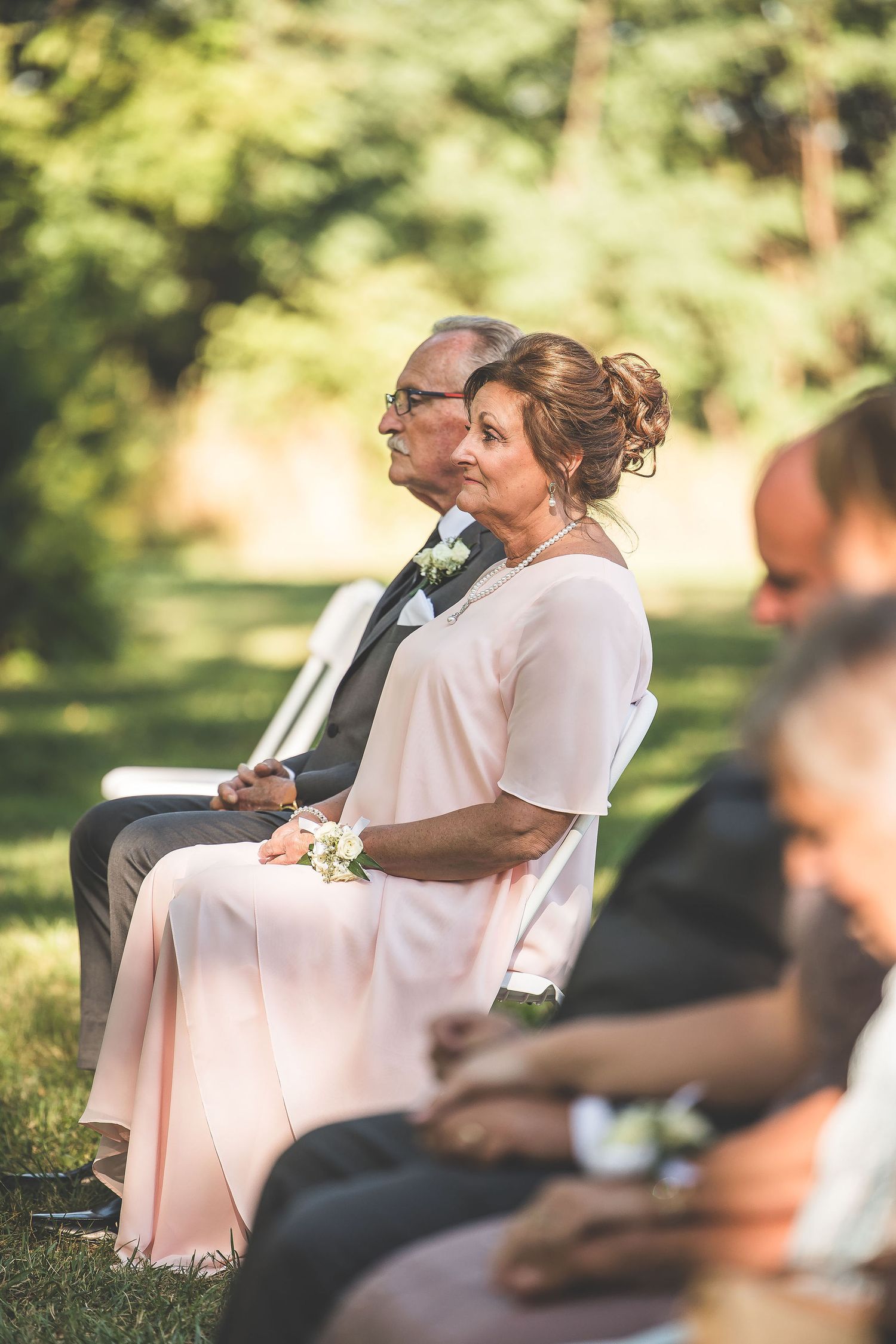 Wedding guests seated in formal attire watching outdoor ceremony.