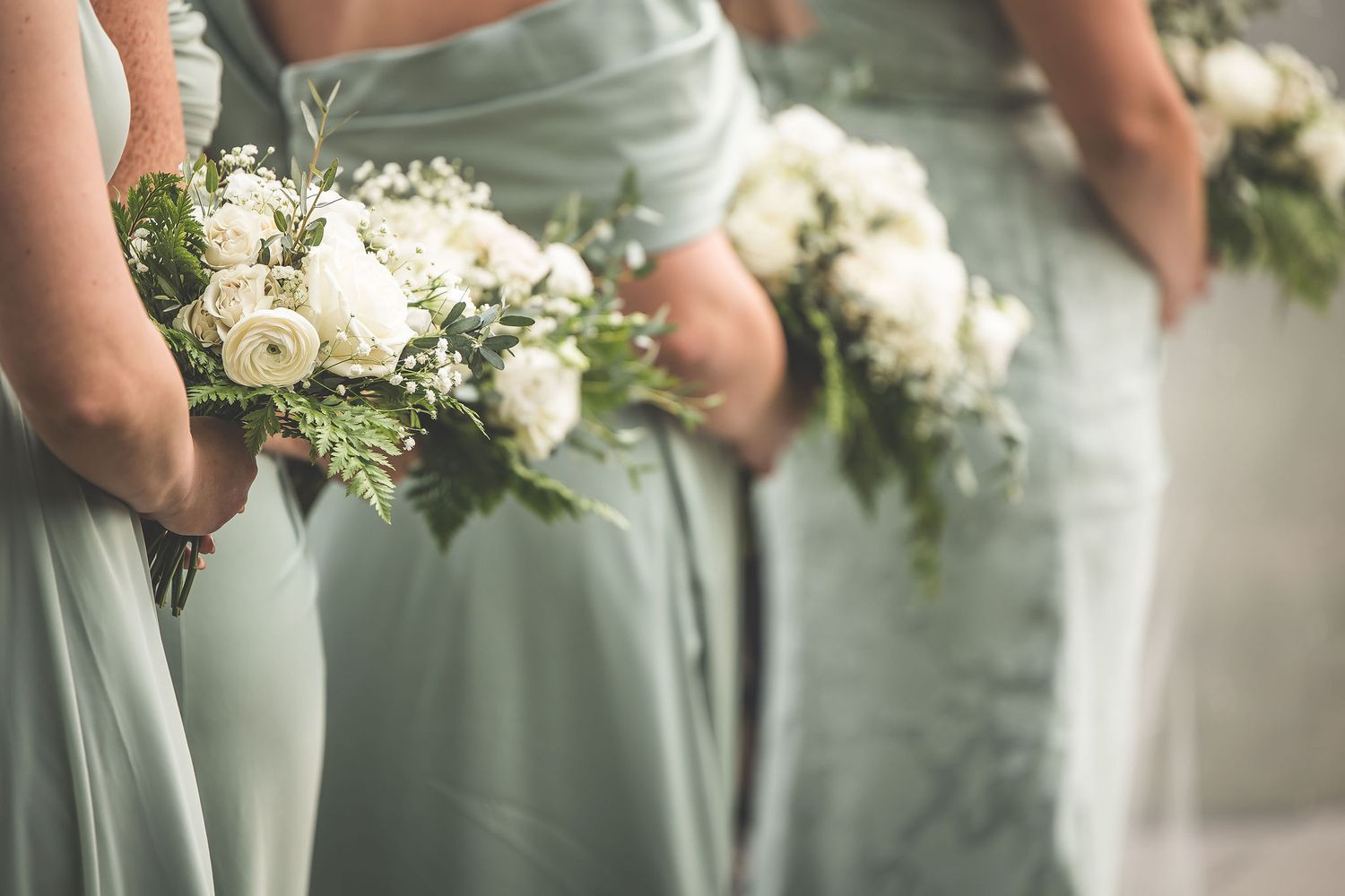 Bridesmaids in sage green dresses hold white floral bouquets.