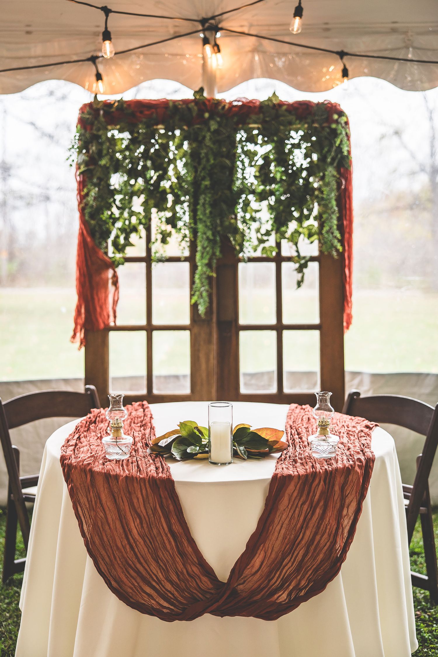 Wedding reception tent with brown chair covers and white tablecloths decorated with red accents.