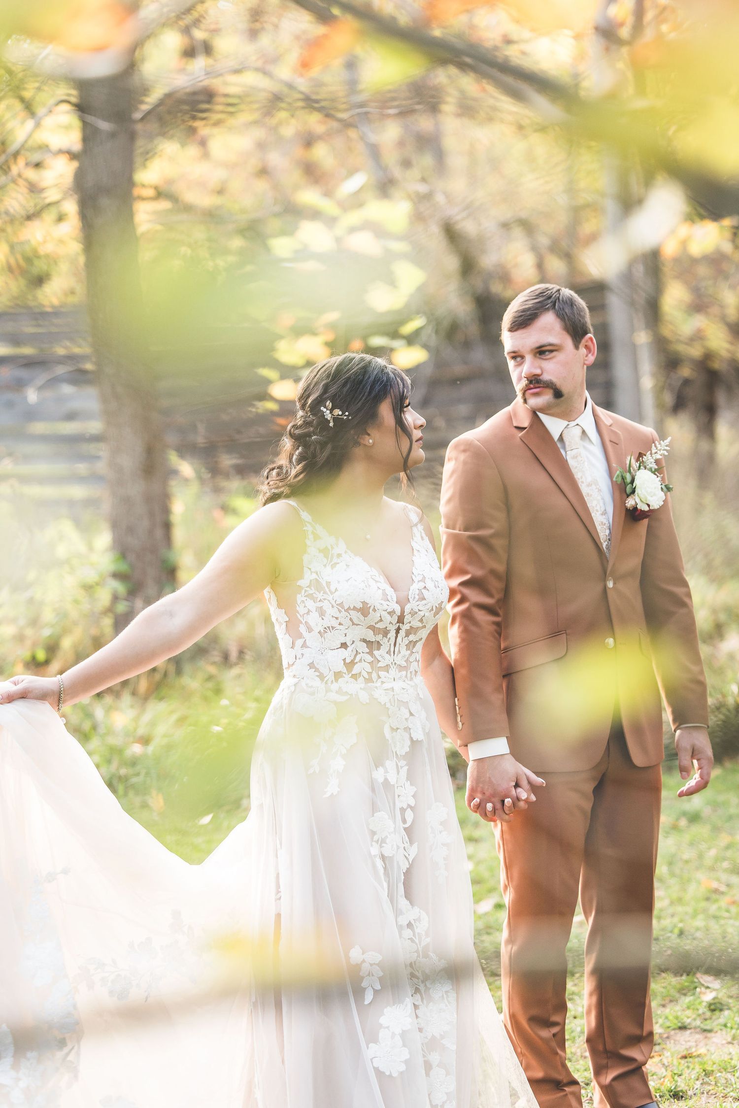 Wedding couple holds hands and walks through a dreamy autumn garden with golden sunlight.