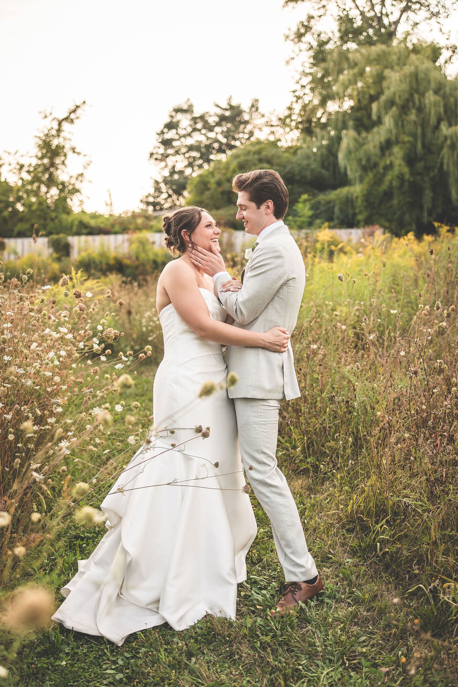 Wedding couple dances playfully in a wildflower field during sunset.