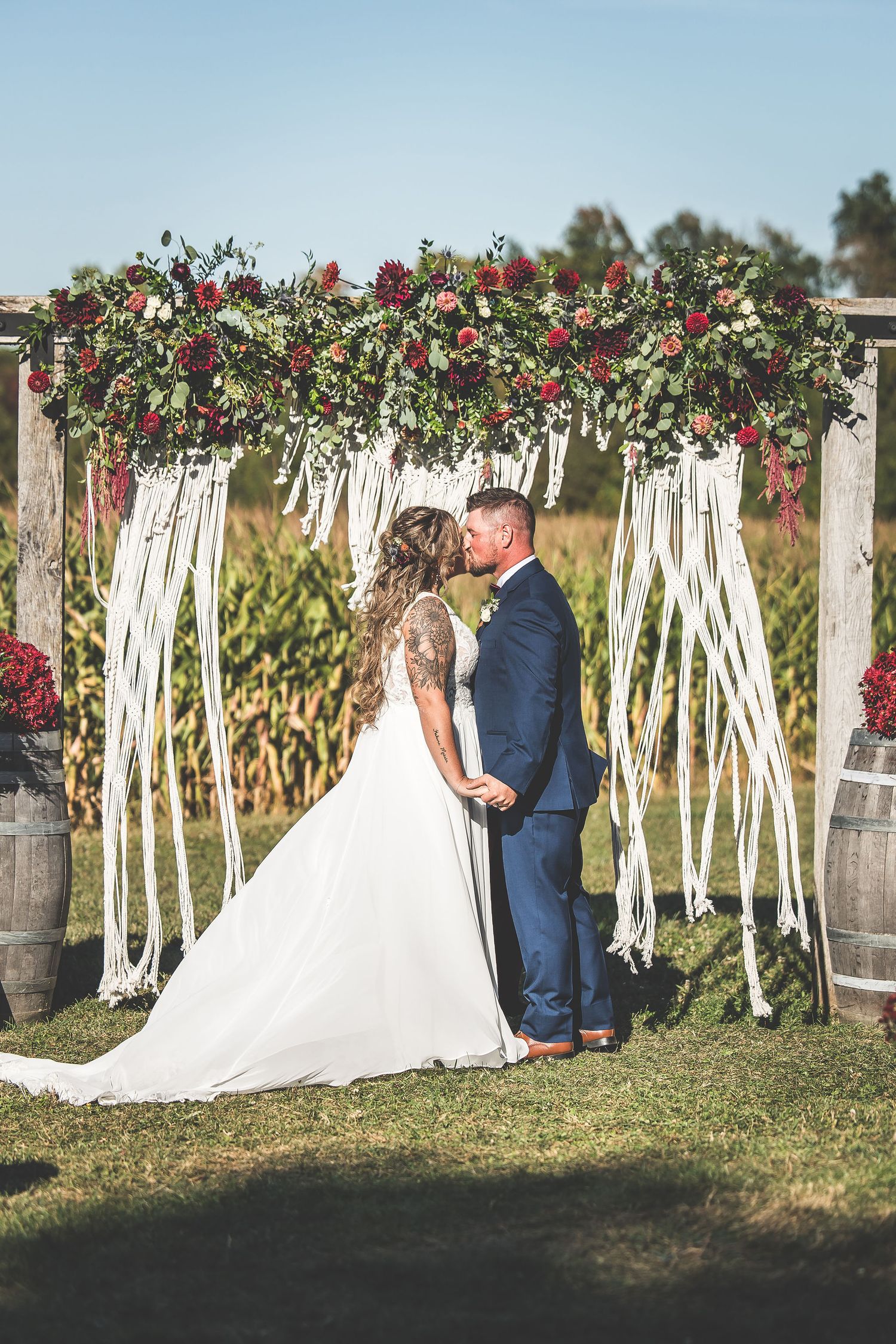 Couple poses romantically in front of a rustic wedding backdrop decorated with white ribbons and red flowers.