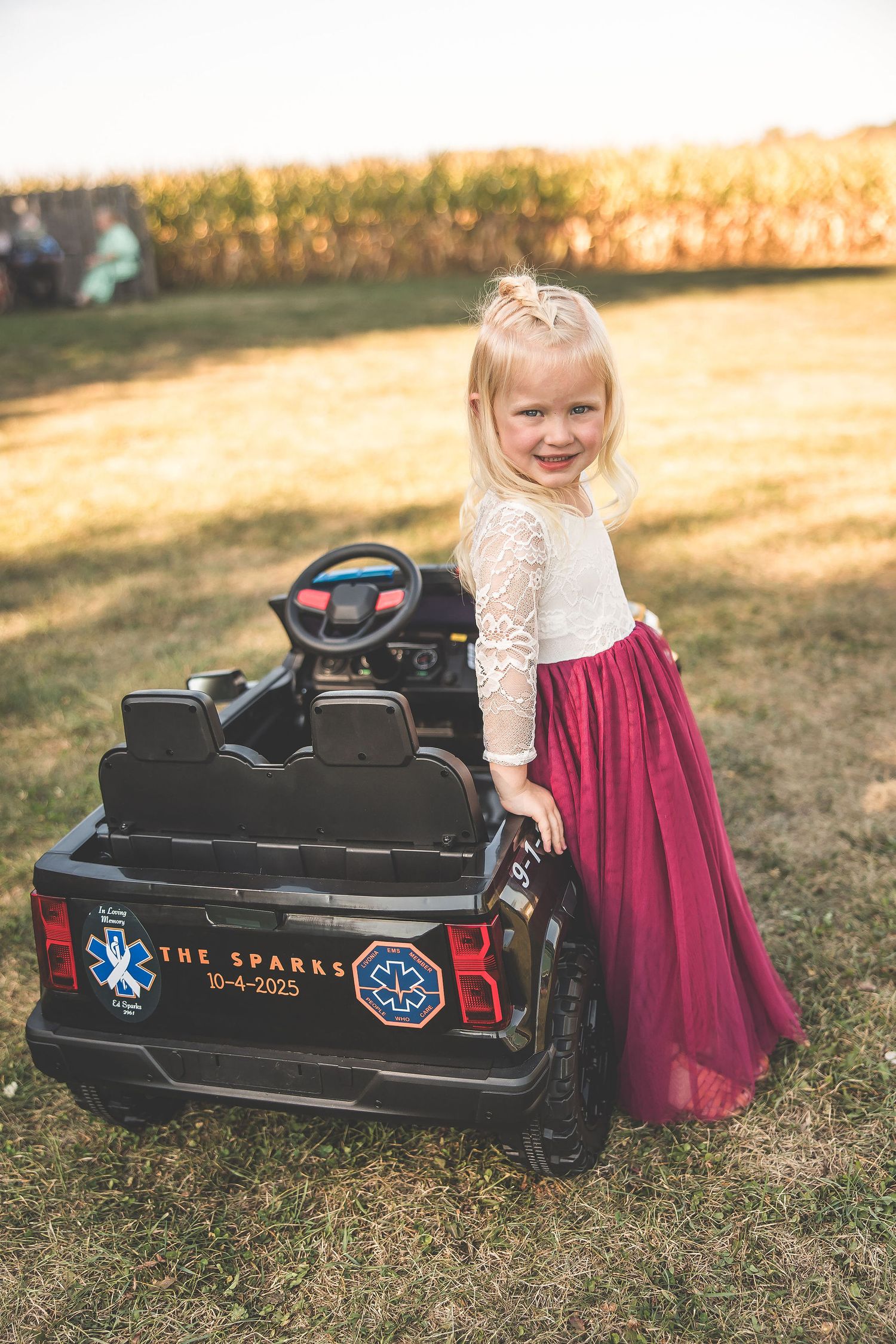 Black toy train car sits on grass during outdoor photoshoot with burgundy and white dress details.