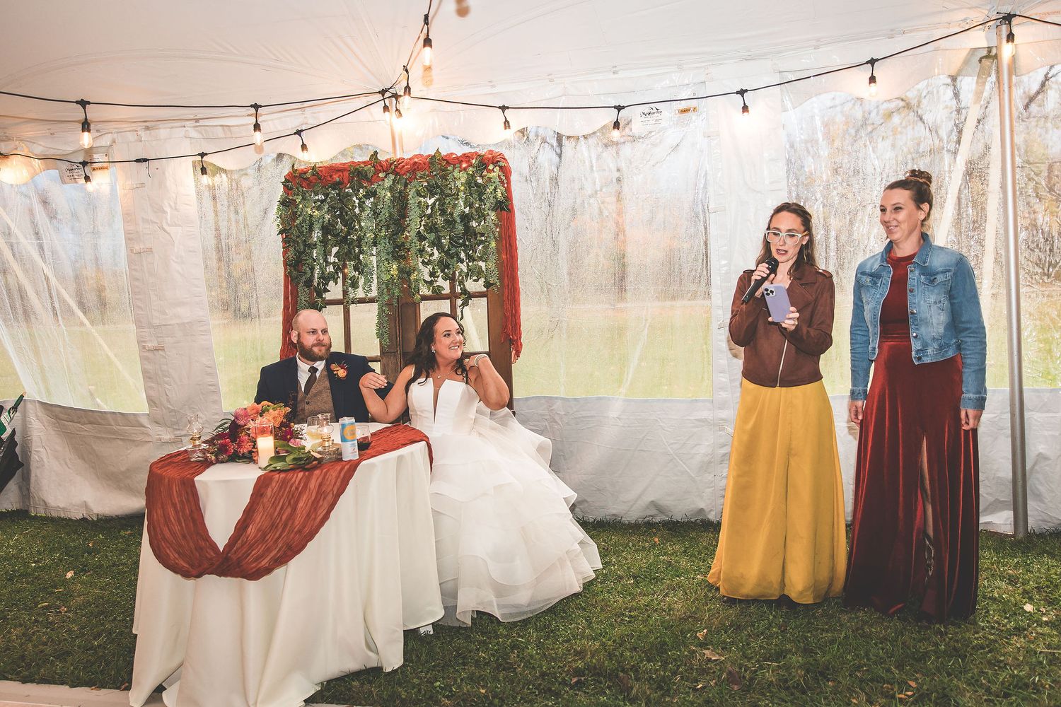 Wedding reception venue decorated with string lights and white fabric in an outdoor tent setting.
