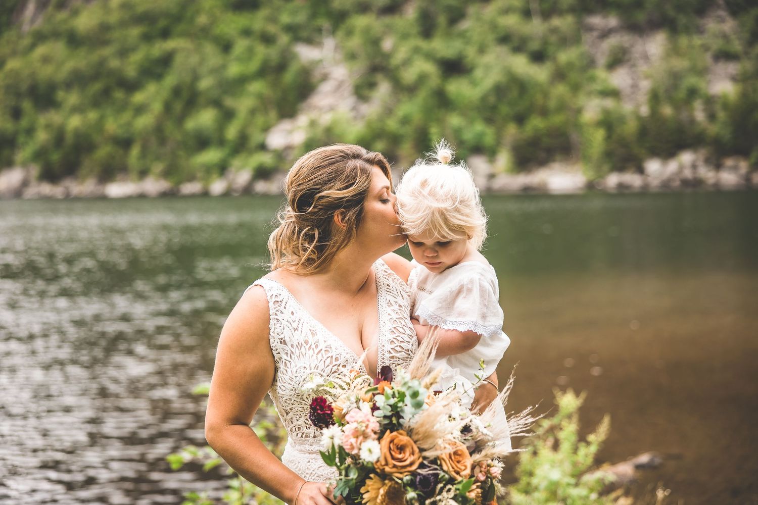 Wedding party poses along rocky shoreline with mountain backdrop.