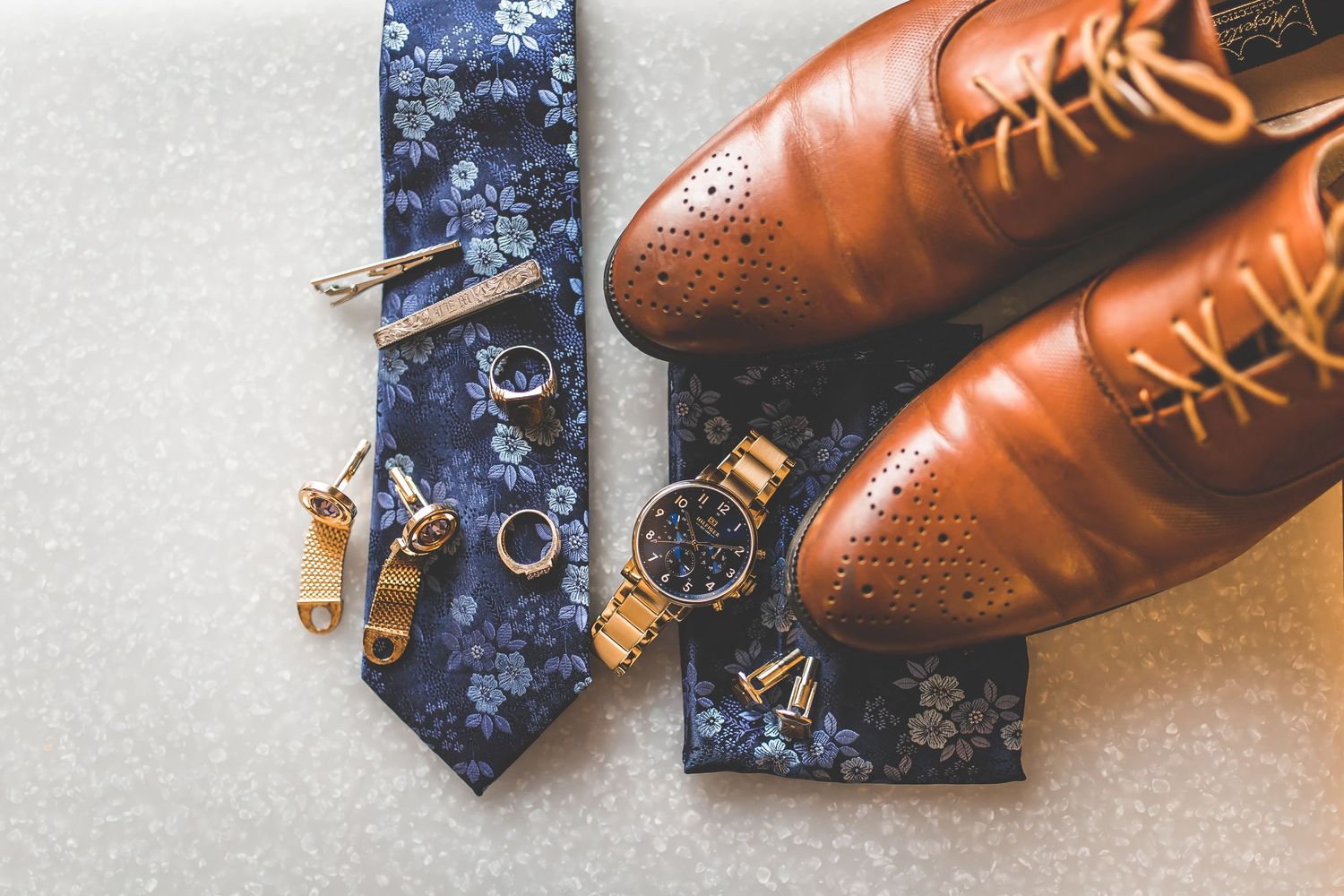 Wedding accessories including brown leather dress shoes, navy tie, and gold cufflinks.