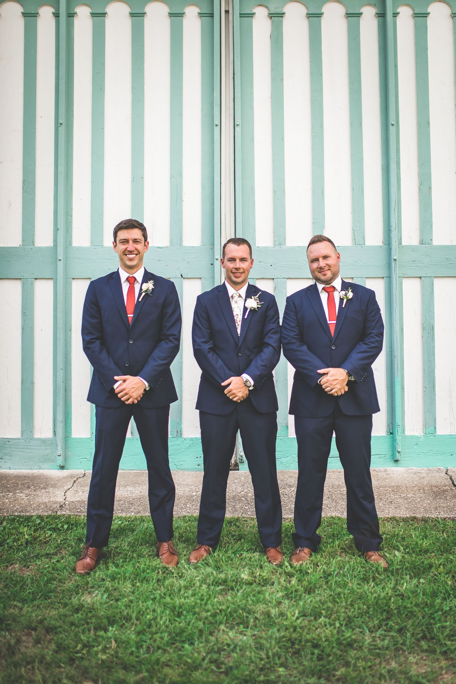 Groomsmen in navy suits with red ties pose sitting against mint green striped wall.