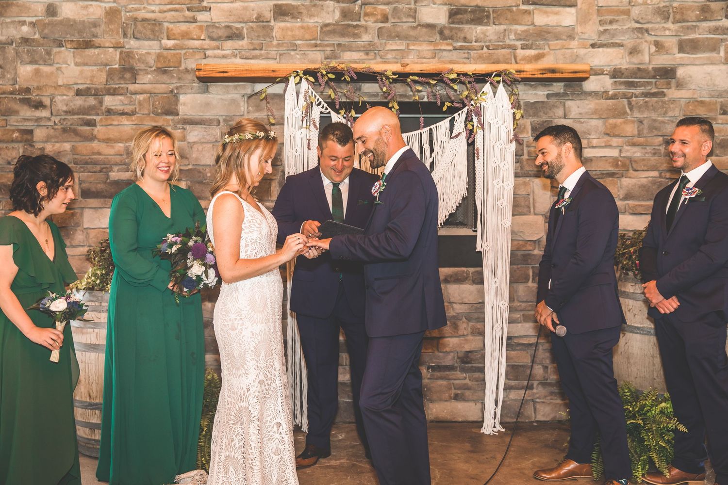 Wedding party poses in front of rustic stone wall with white fabric draping and floral decorations.
