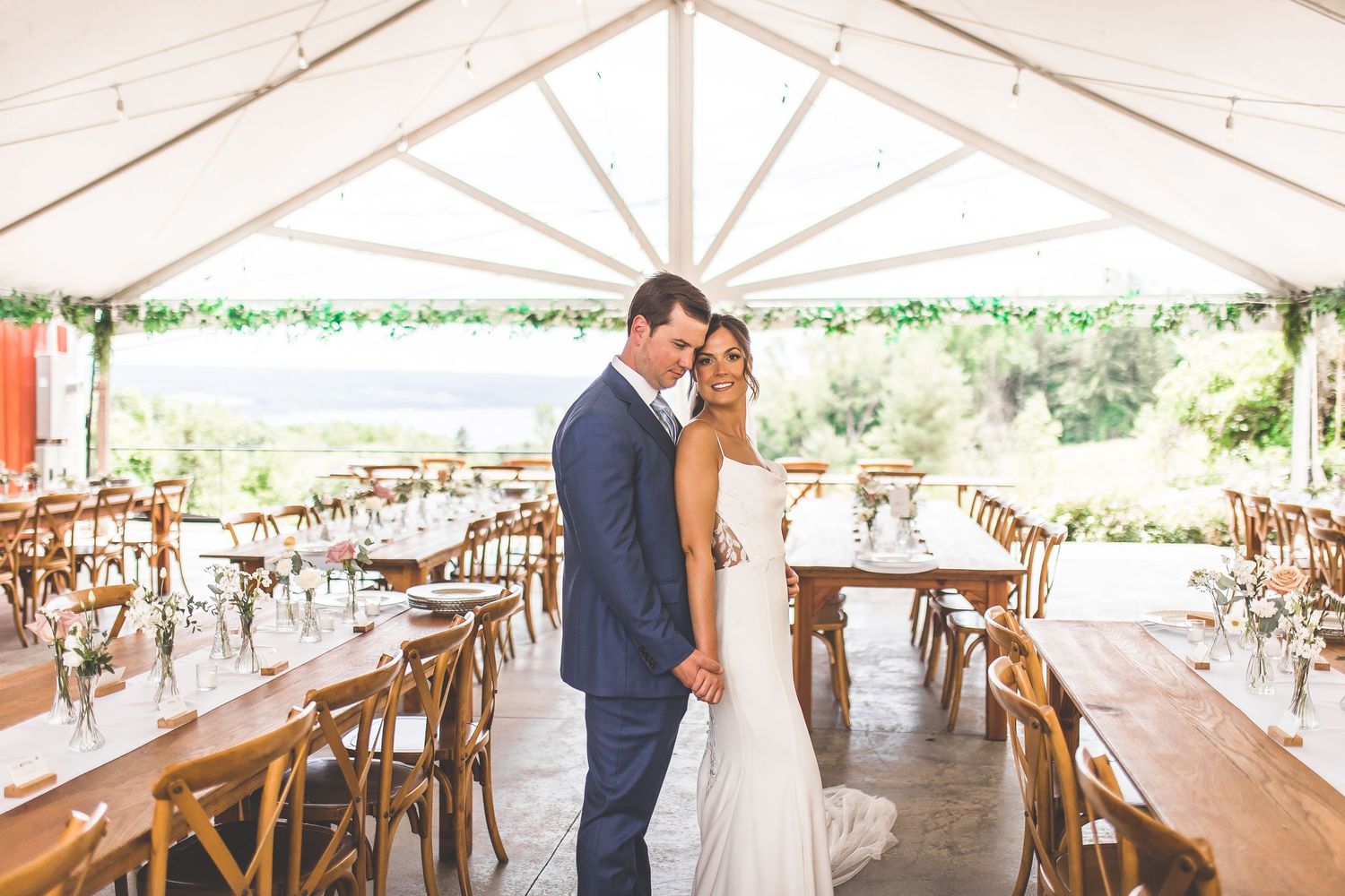 Wedding reception setup with wooden chairs and tables under an elegant white tent.