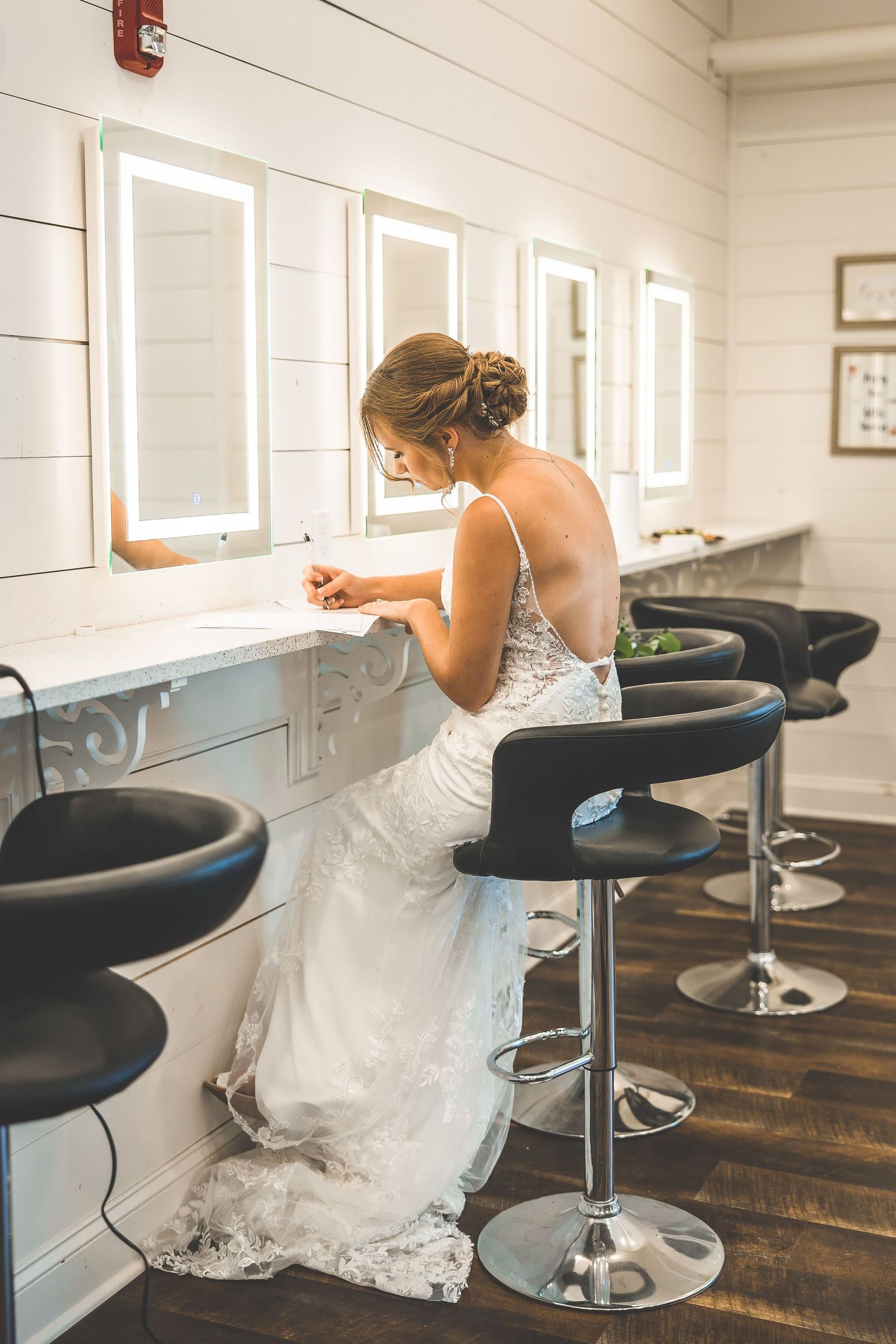 A white wedding dress flows over a modern black bar stool in a bright indoor setting.