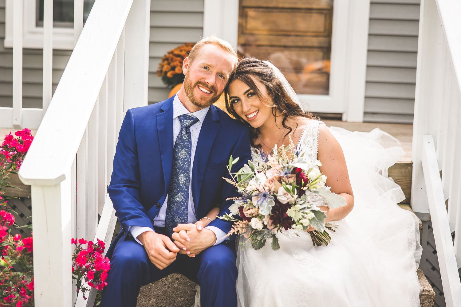 Wedding couple sharing intimate moments on a white porch with gray siding and pink flowers.