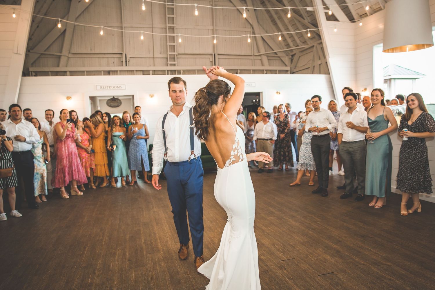 Wedding reception dance floor moments captured in a rustic indoor venue with high ceilings.