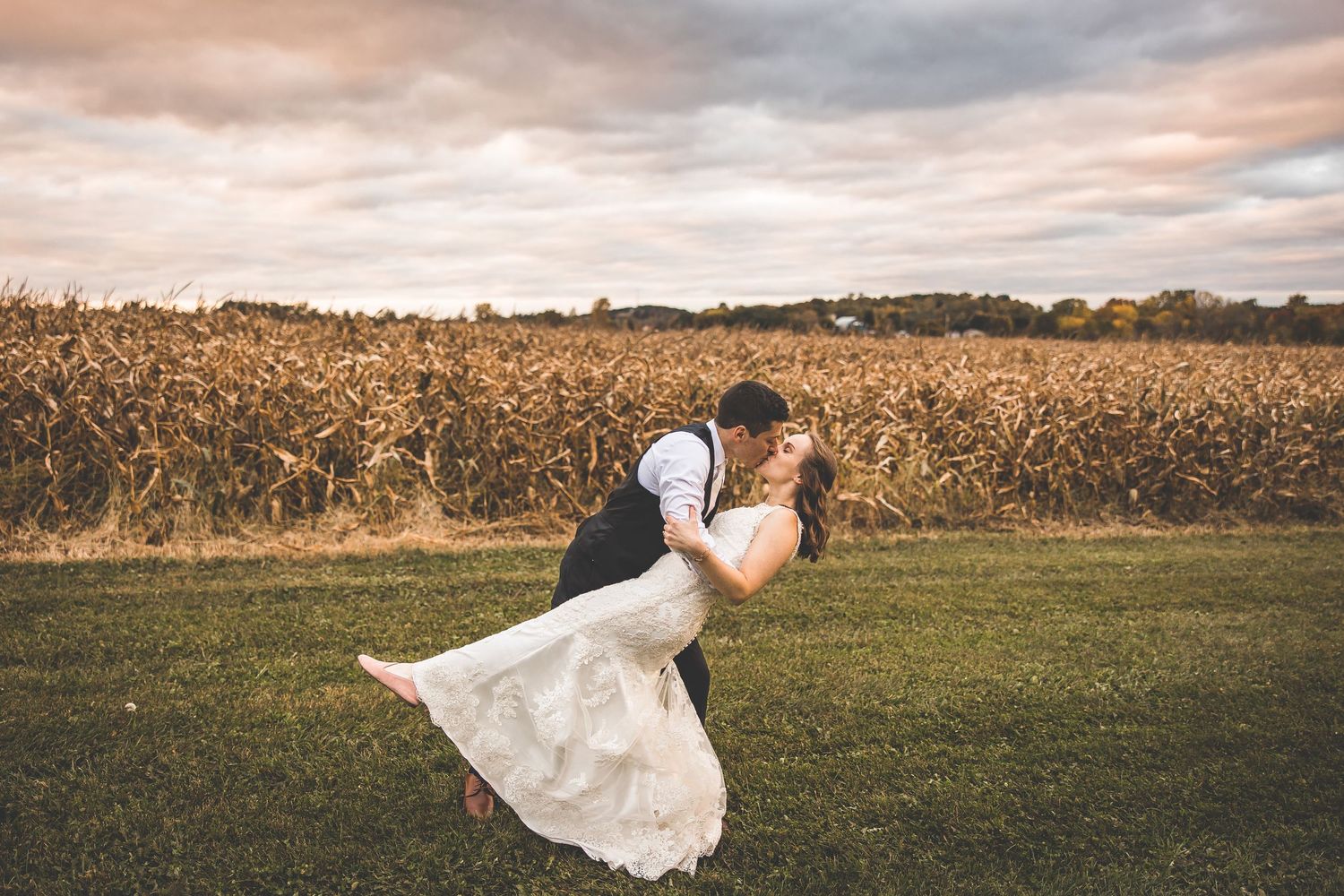 Panoramic view of newlyweds in autumn field with dramatic sunset sky.