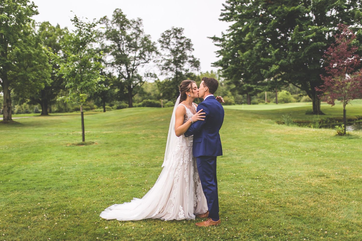 A tender embrace between newlyweds on a beautiful green lawn surrounded by trees.