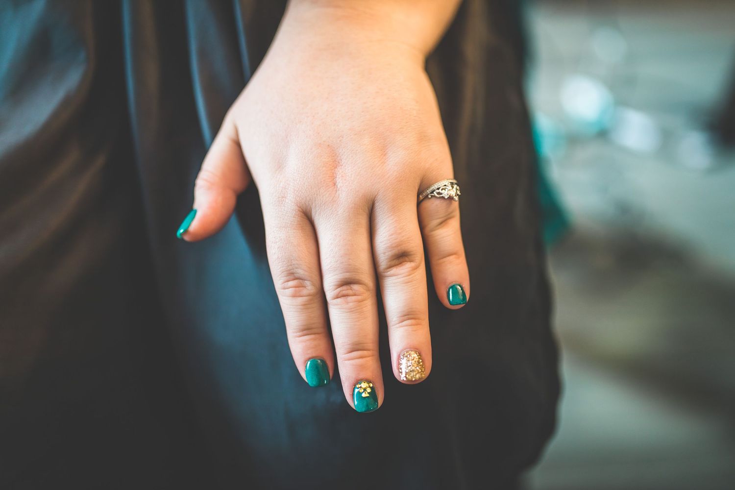 Hands with emerald green nail polish and gold glitter details.