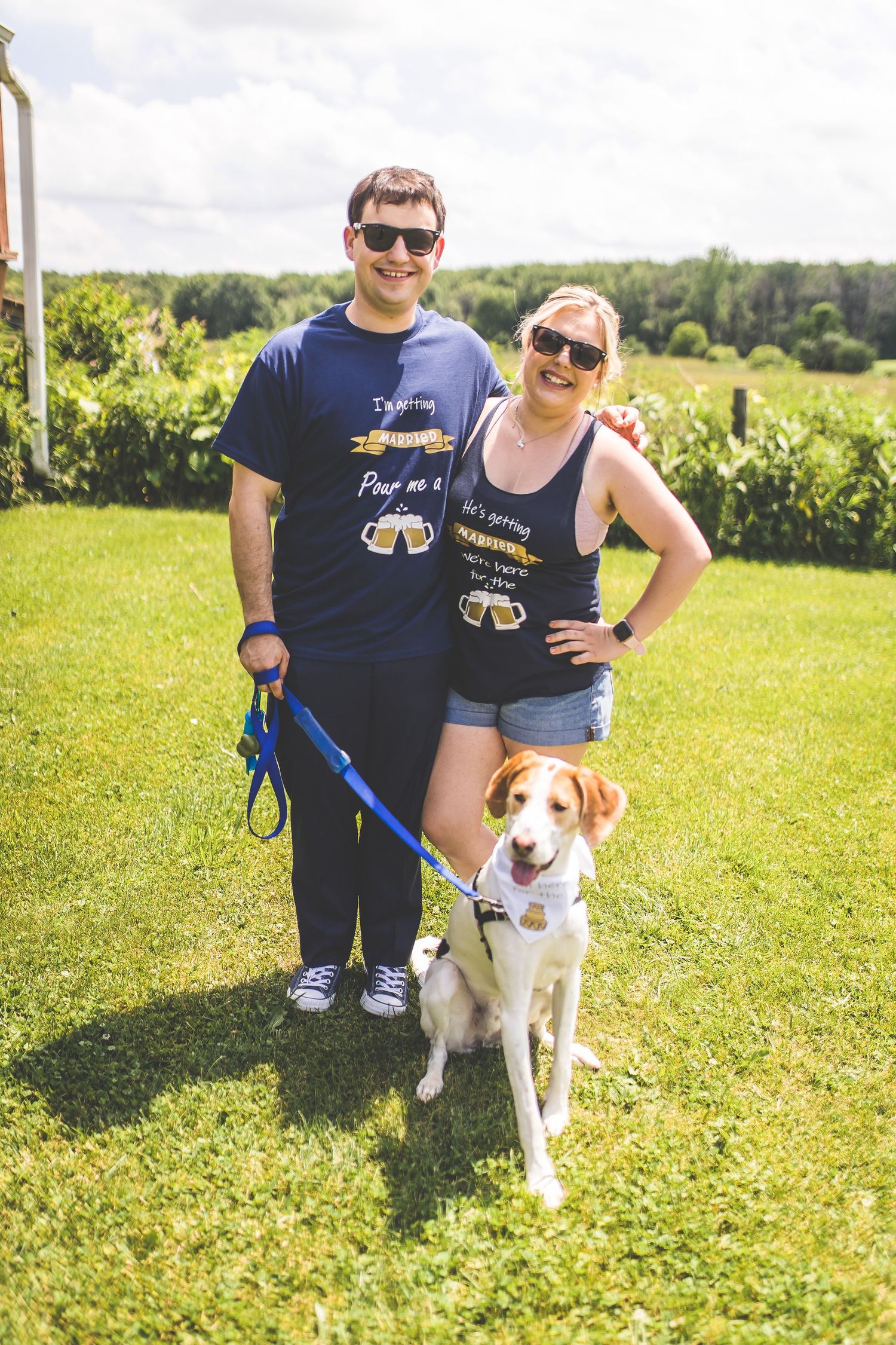 Couple poses with their beagle dog in matching navy outfits on sunny lawn.