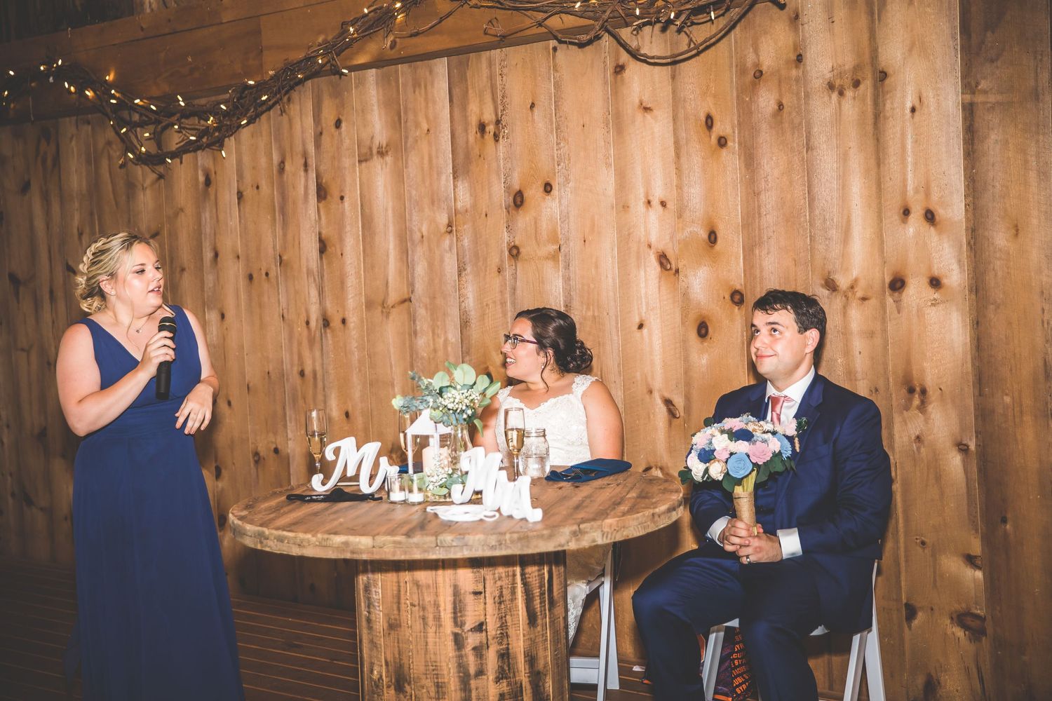 Wedding reception celebration in a barn venue with wooden walls and decorative lighting.