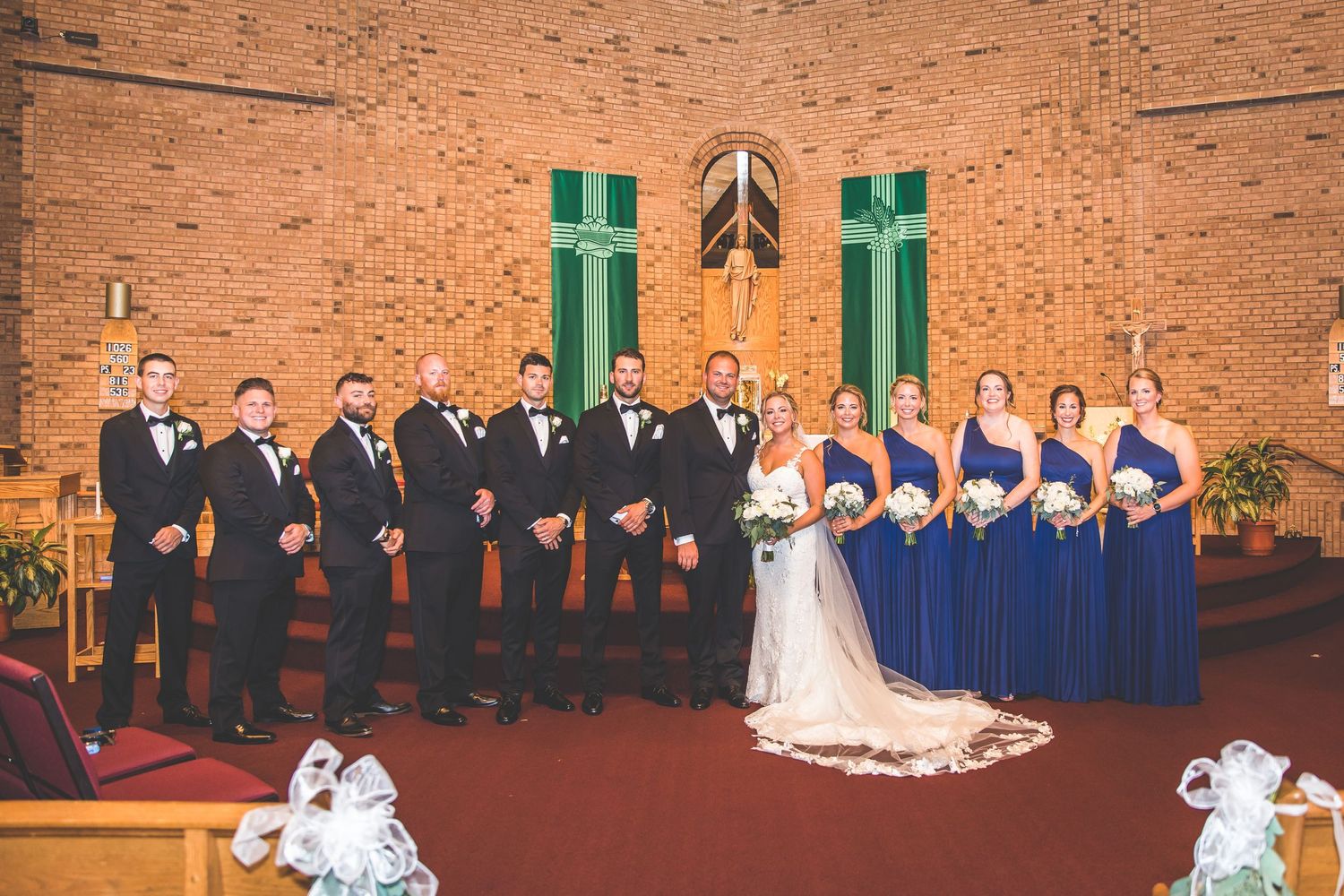 Wedding party lineup in formal attire against brick church backdrop with blue and black color scheme.