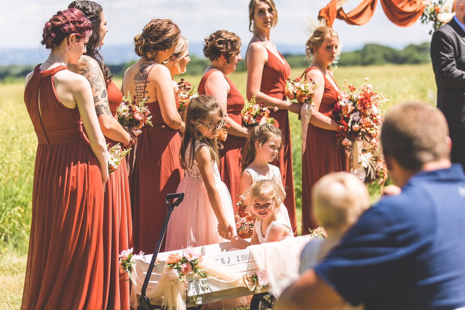 Bridesmaids in rust-colored dresses holding bouquets at outdoor ceremony.