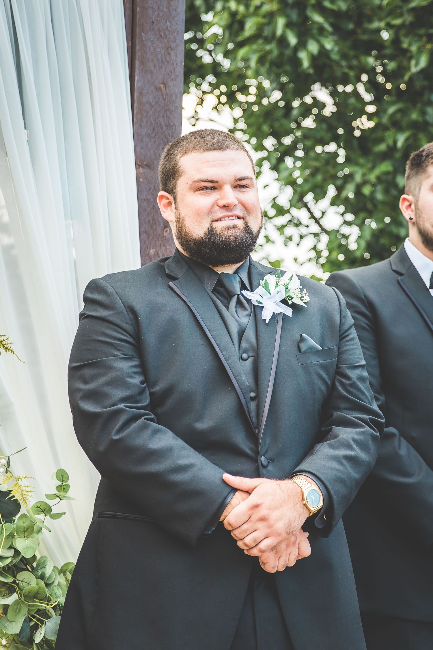 Groomsmen in black suits standing in formation during an outdoor wedding ceremony.