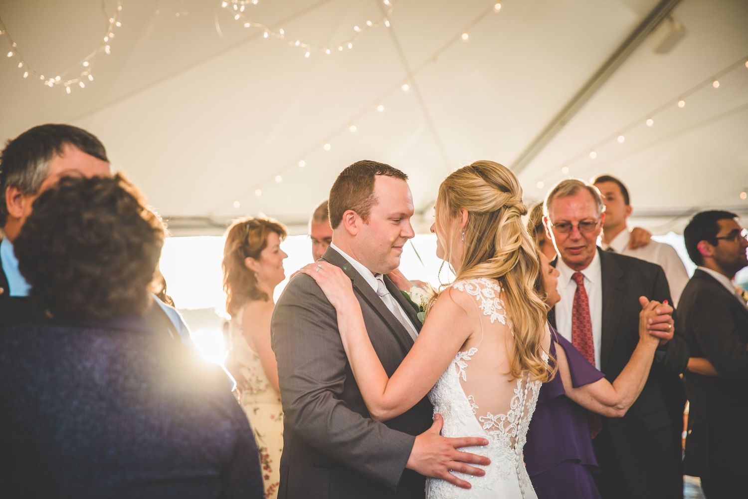 Couples dancing at a wedding reception under twinkling lights in a tent.