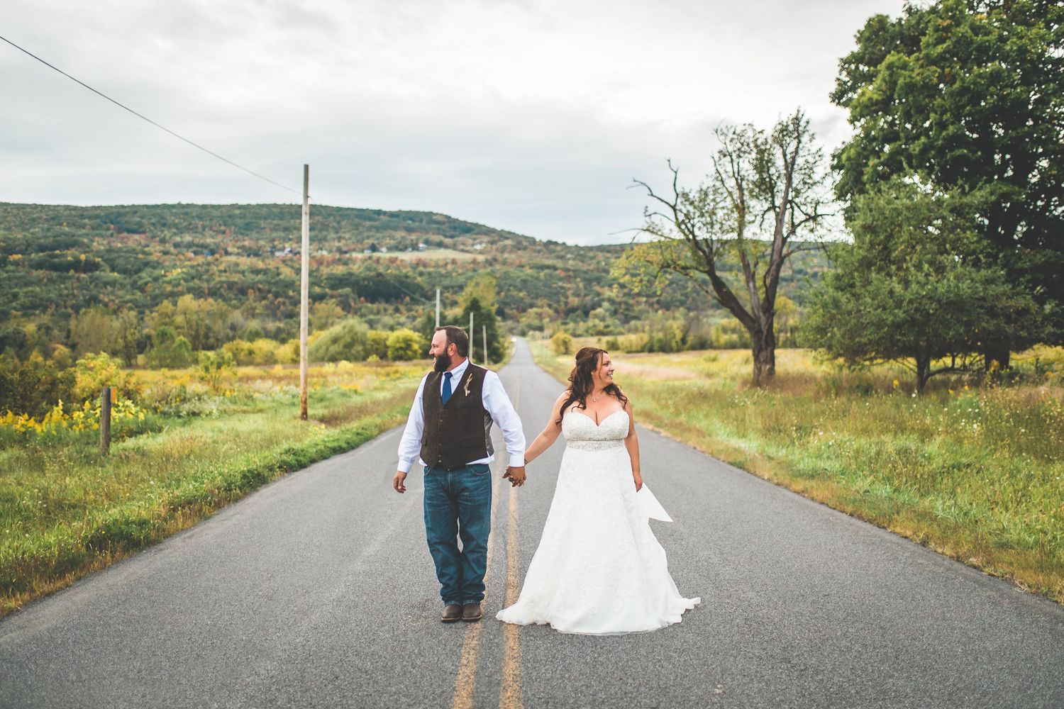 Couple walks together on a country road with rolling hills in the background.