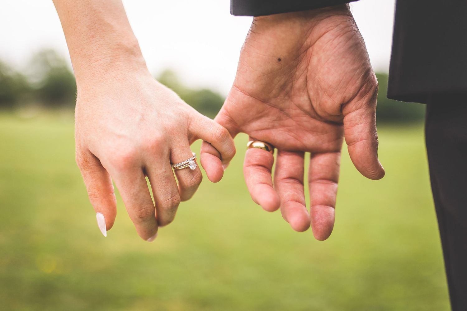 Close-up of newlyweds holding hands showing wedding rings and manicured nails.