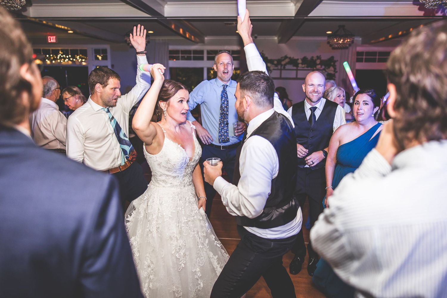 Wedding guests dancing and celebrating under colorful party lights at indoor reception.