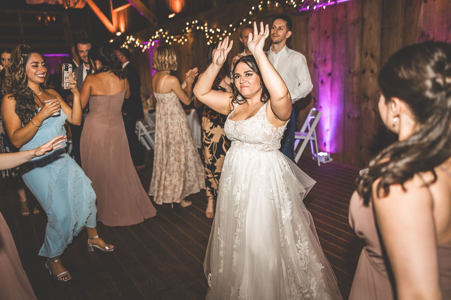 Wedding reception dance floor filled with guests enjoying celebration in barn venue.