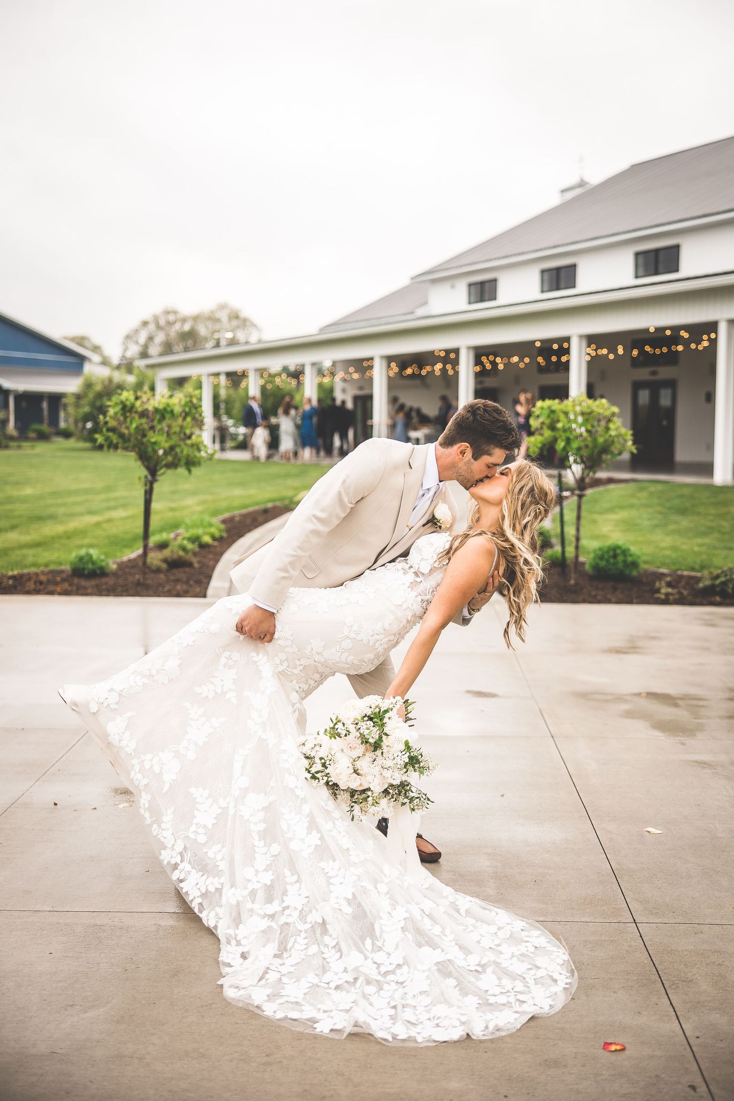 Romantic dip pose of newlyweds with flowing lace train against venue backdrop.