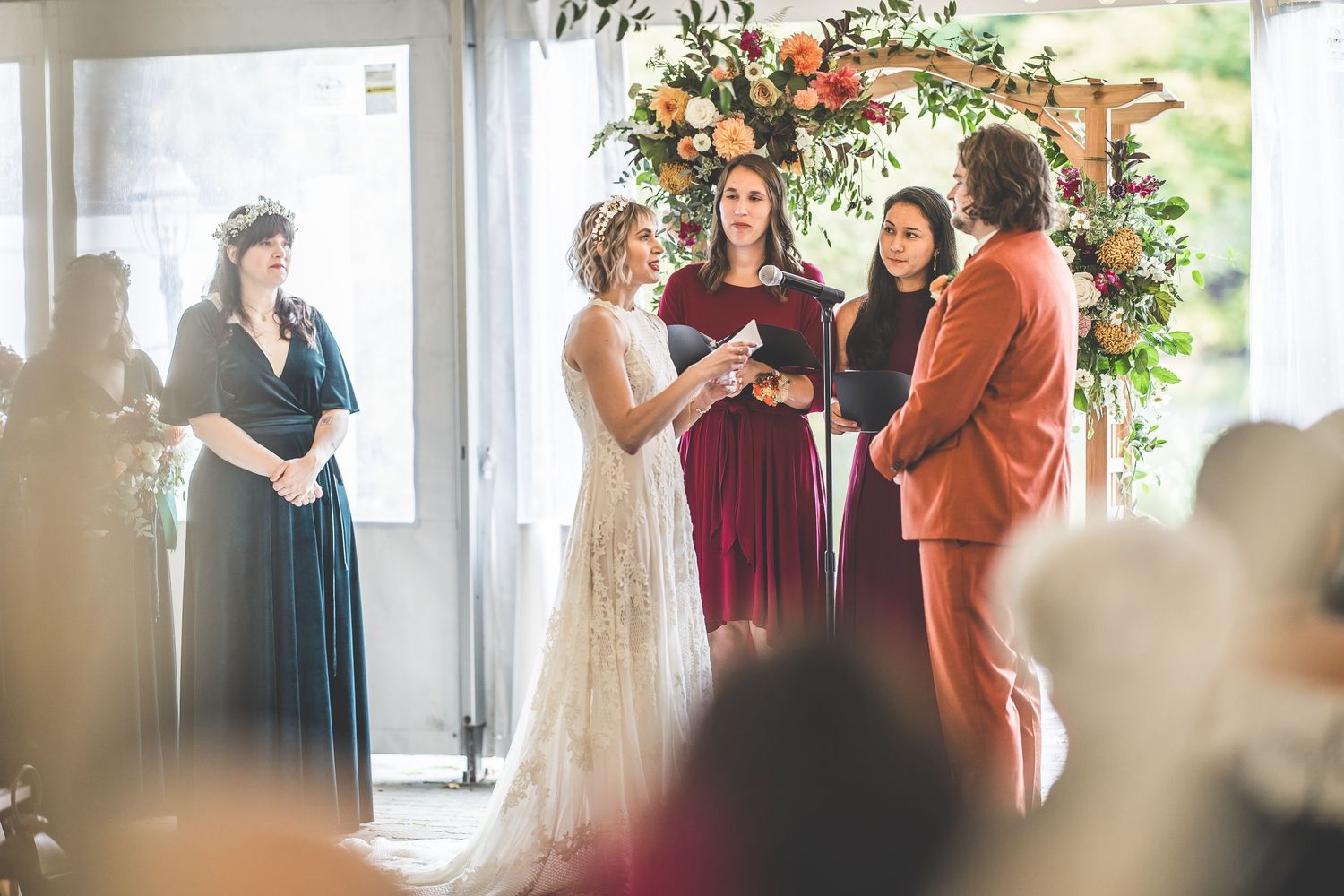 Indoor wedding ceremony with burgundy and rust color scheme under elegant floral arrangements.