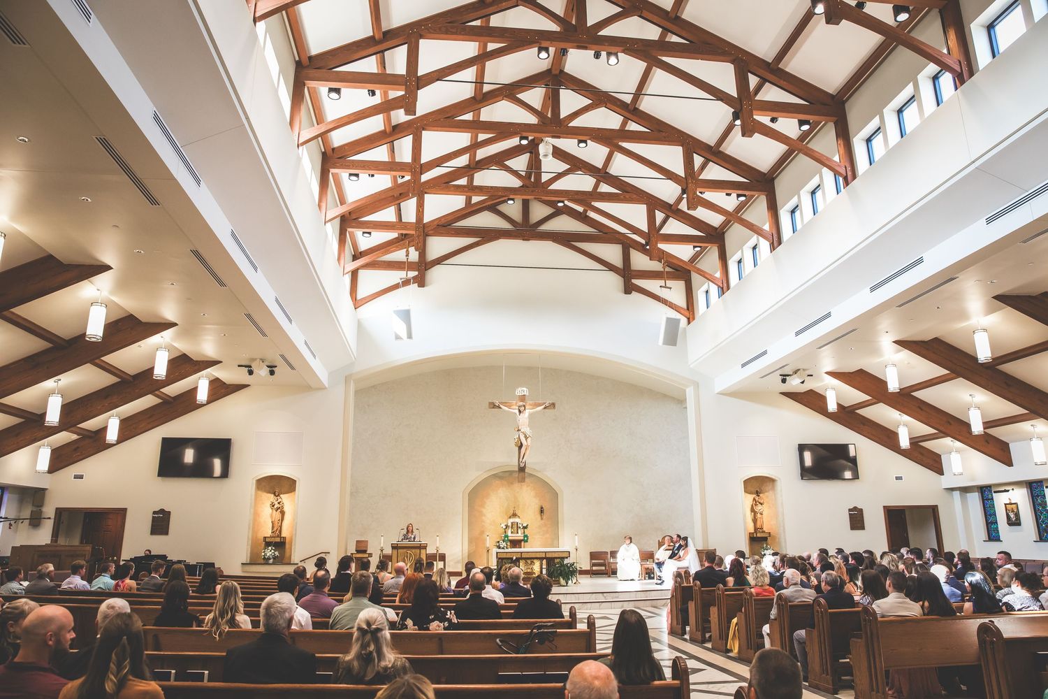 Church sanctuary with exposed wooden beams and skylights during a wedding service.