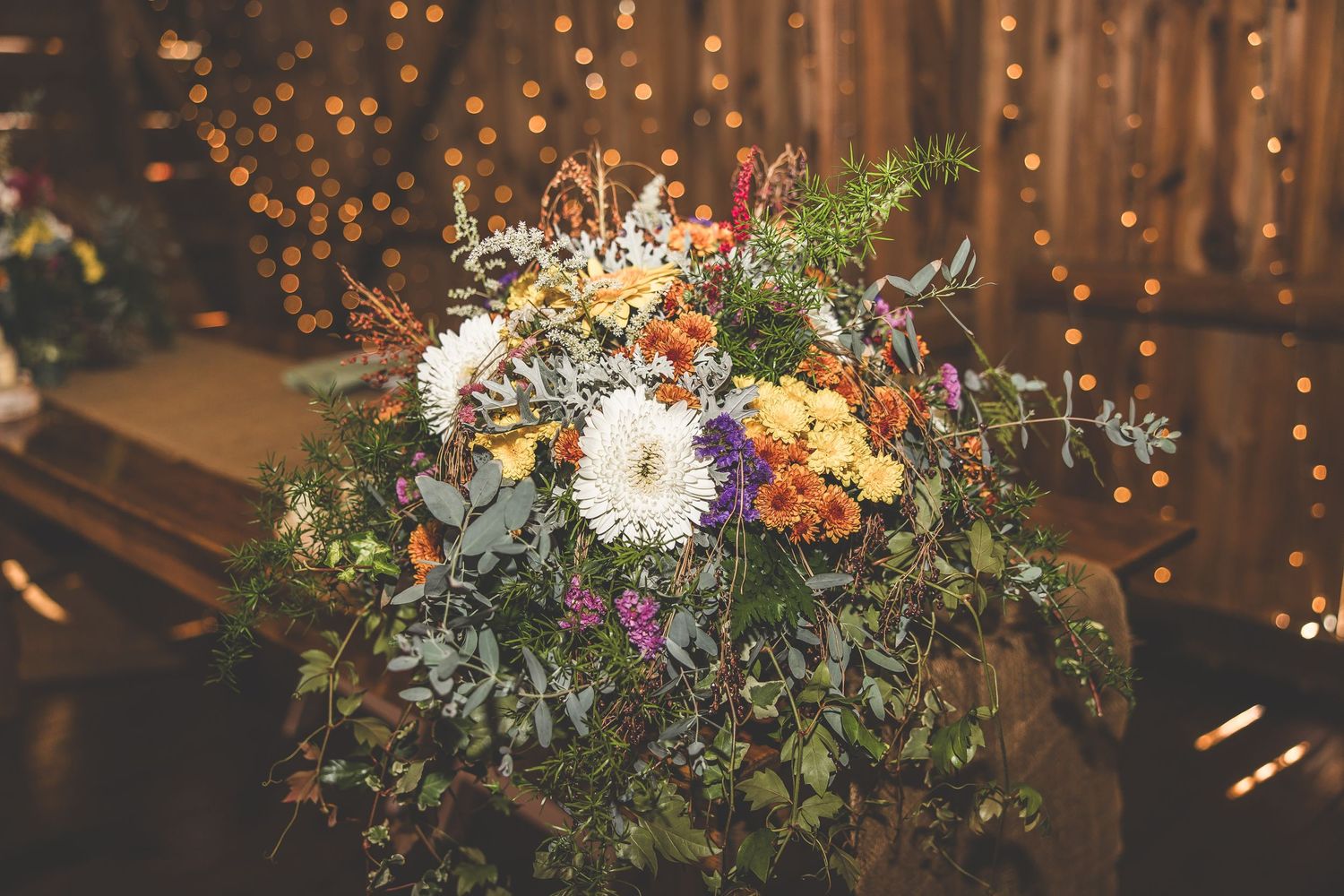 Fall-themed floral arrangement with orange and white blooms against twinkle lights.