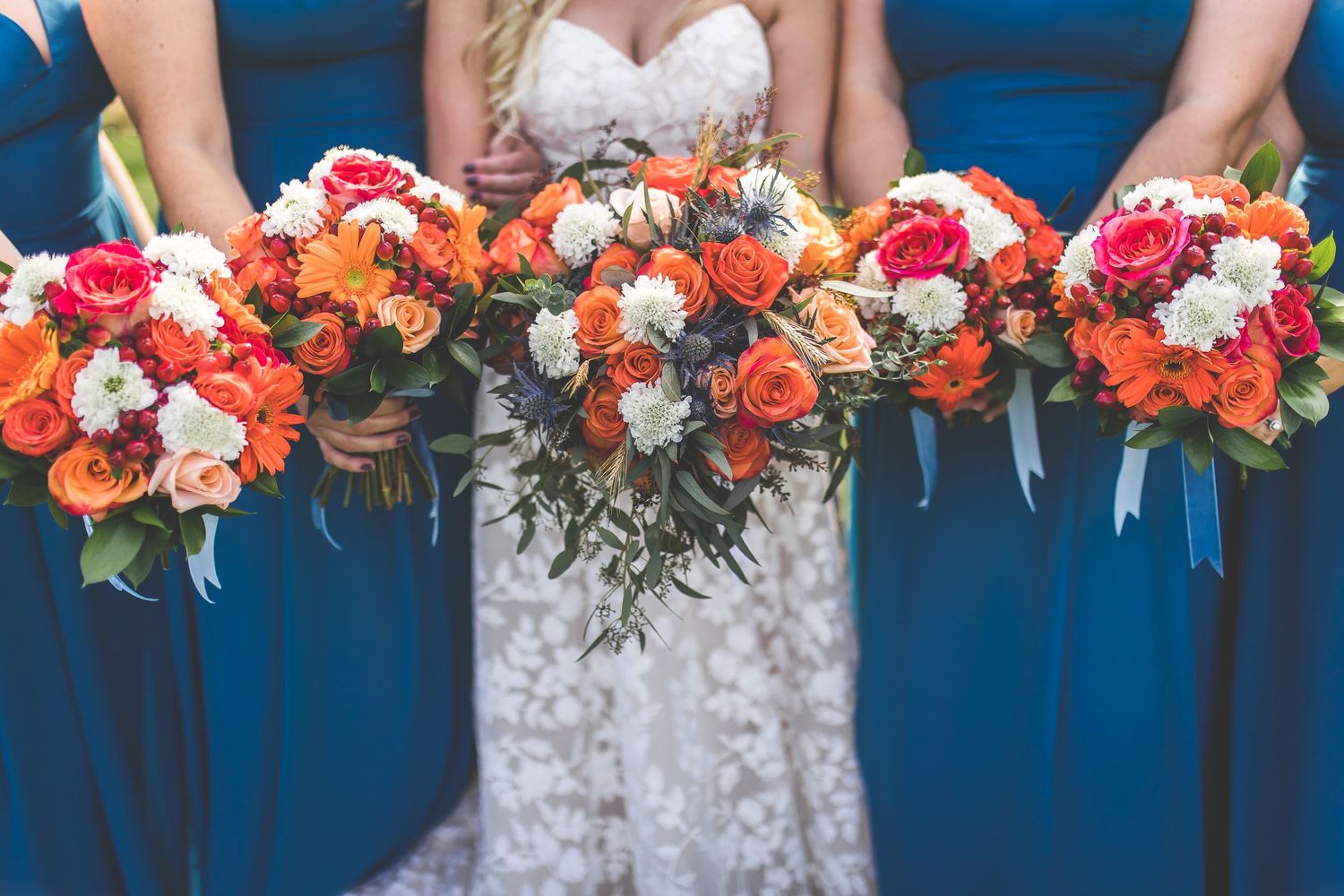 Close-up of wedding bouquets with red and orange flowers held against navy blue dresses.