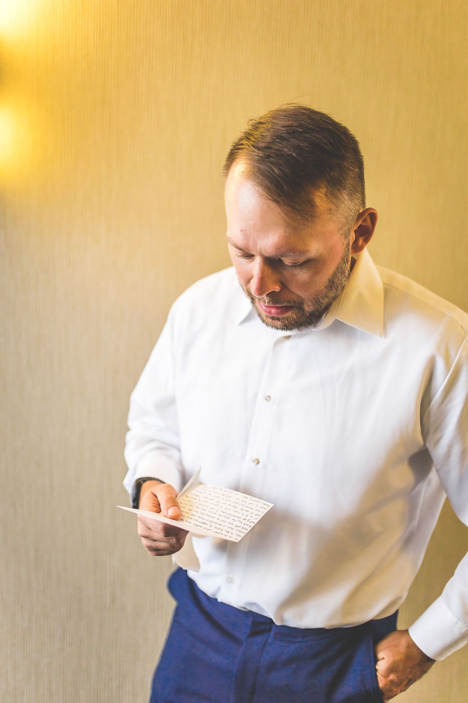 Person in white shirt and navy pants reading a note or card.